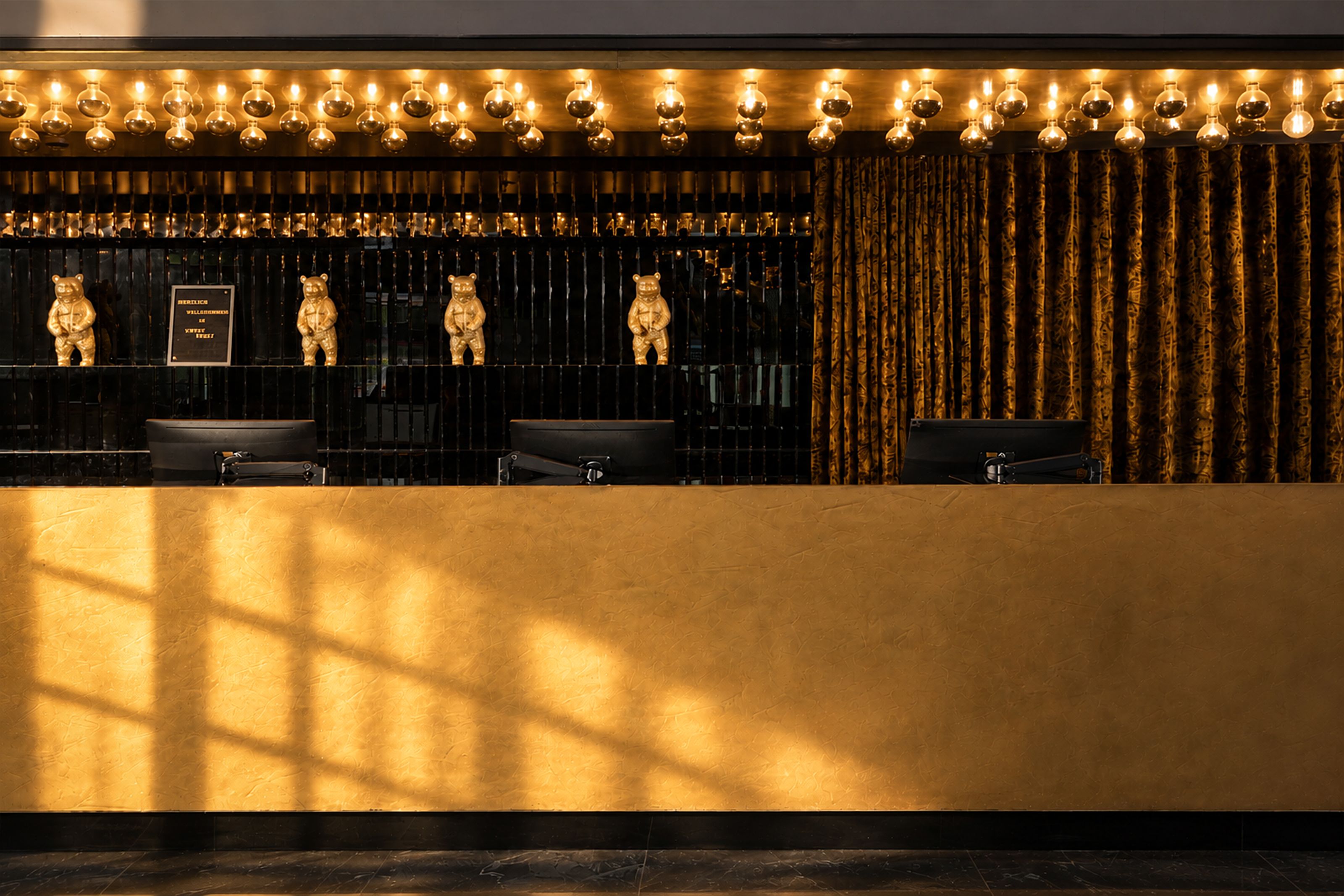 Rezeption mit goldfarbenem Tresen, warmem Licht und stilvoller Deko, darunter mehrere kleine Bärenfiguren, in eleganter, einladender Atmosphäre.