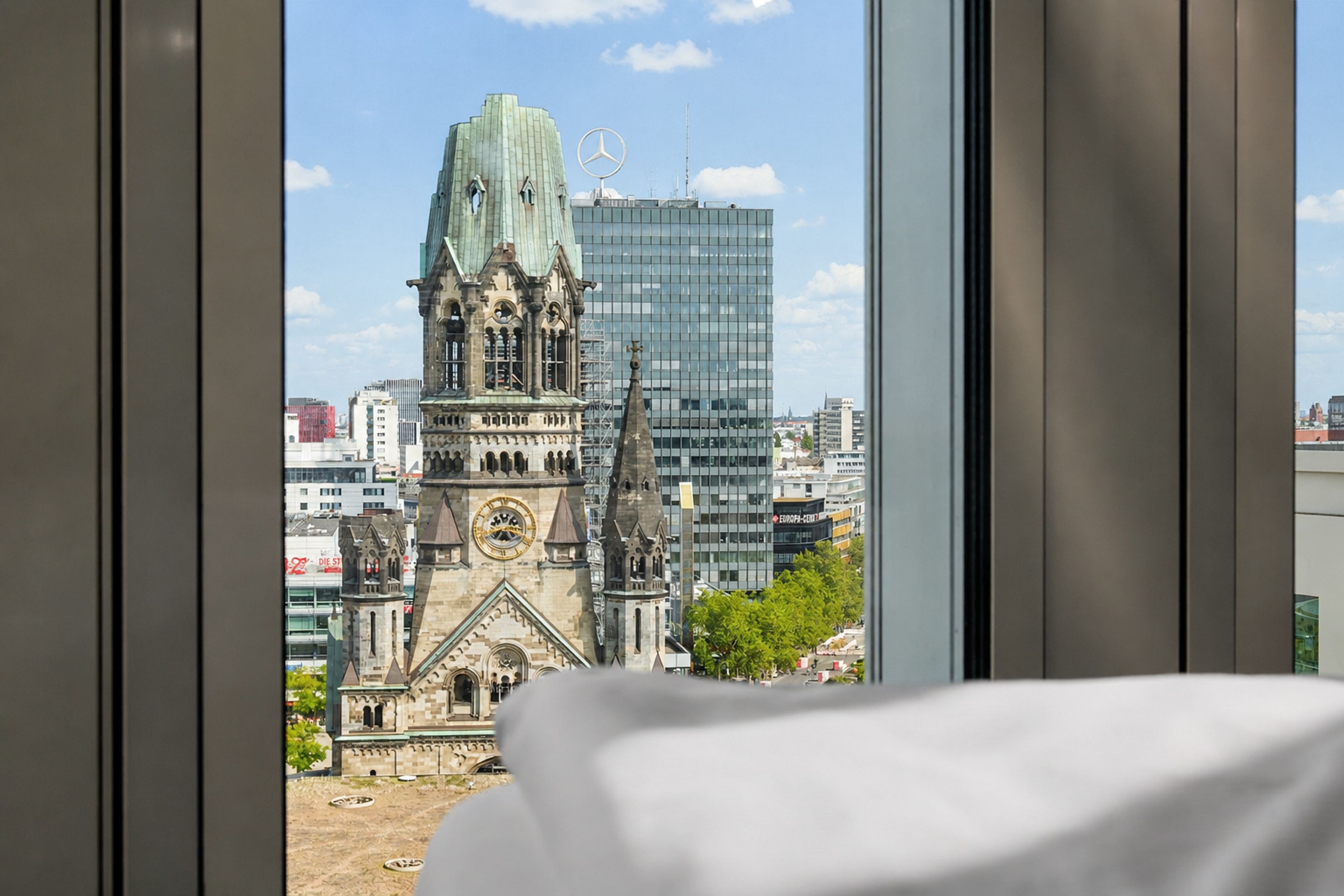 Blick aus einem Hotelzimmerfenster auf die Kaiser-Wilhelm-Gedächtniskirche und moderne Gebäude in der Berliner Innenstadt bei klarem Himmel. Blick aus einem Hotelzimmerfenster auf die Kaiser-Wilhelm-Gedächtniskirche und moderne Gebäude in der Berliner Innenstadt bei klarem Himmel.