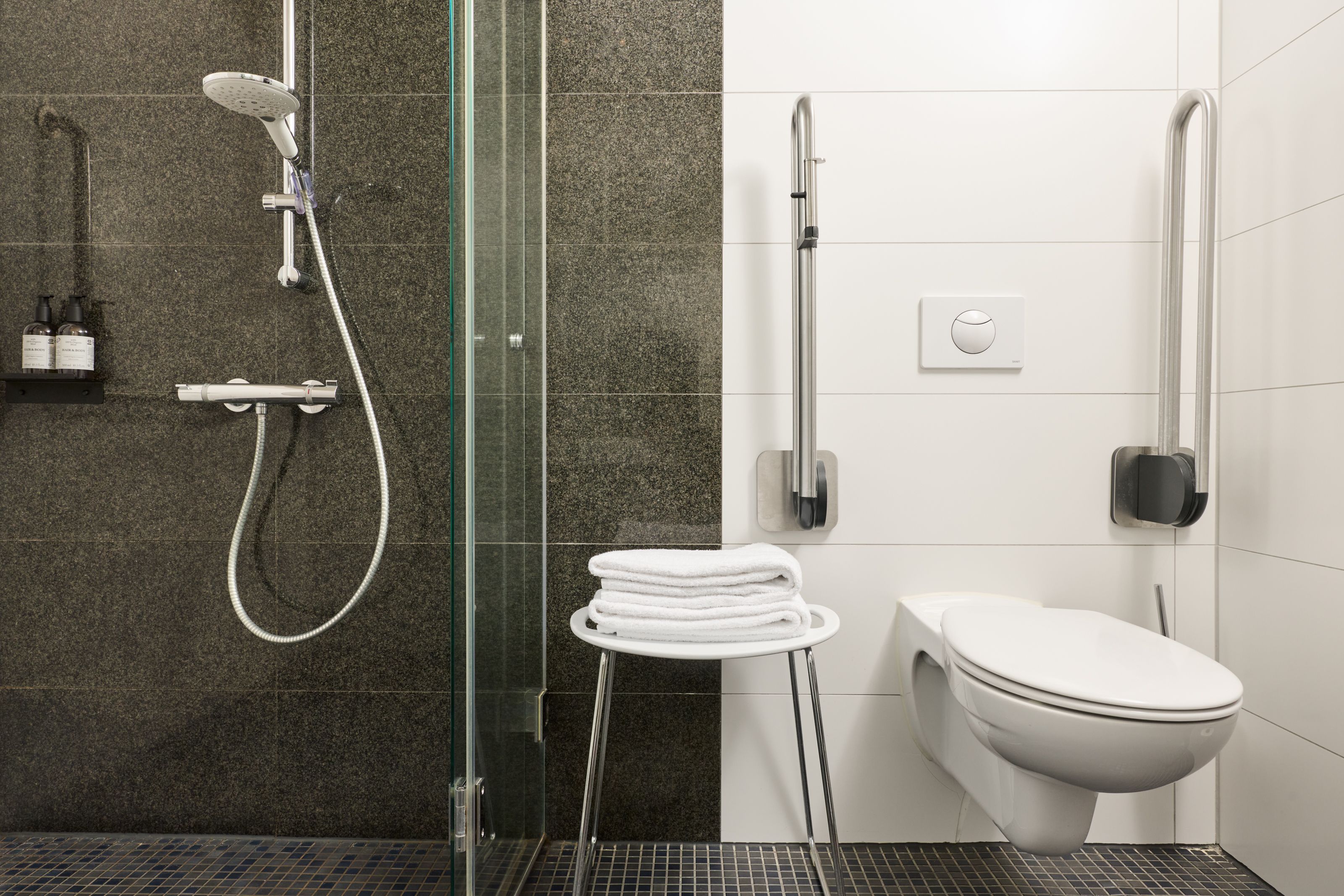 Barrierefreies Badezimmer mit moderner Dusche, Haltegriffen und Toilettenstuhl, ausgestattet für Komfort und Sicherheit.