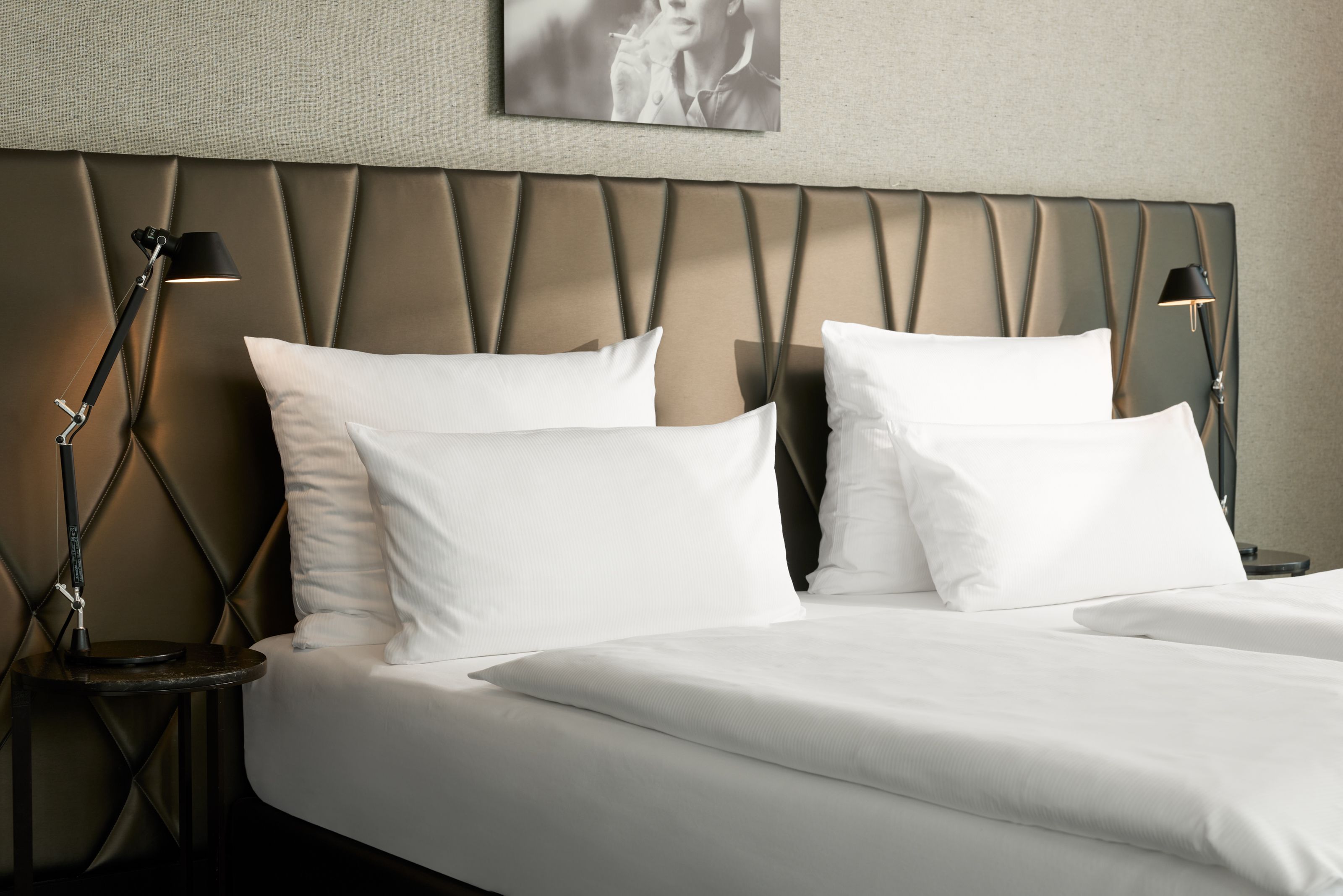 Modernes Doppelbett mit weißer Bettwäsche und gepolstertem Kopfteil in elegantem Hotelzimmer, seitlich zwei Nachttischlampen für gemütliche Beleuchtung.