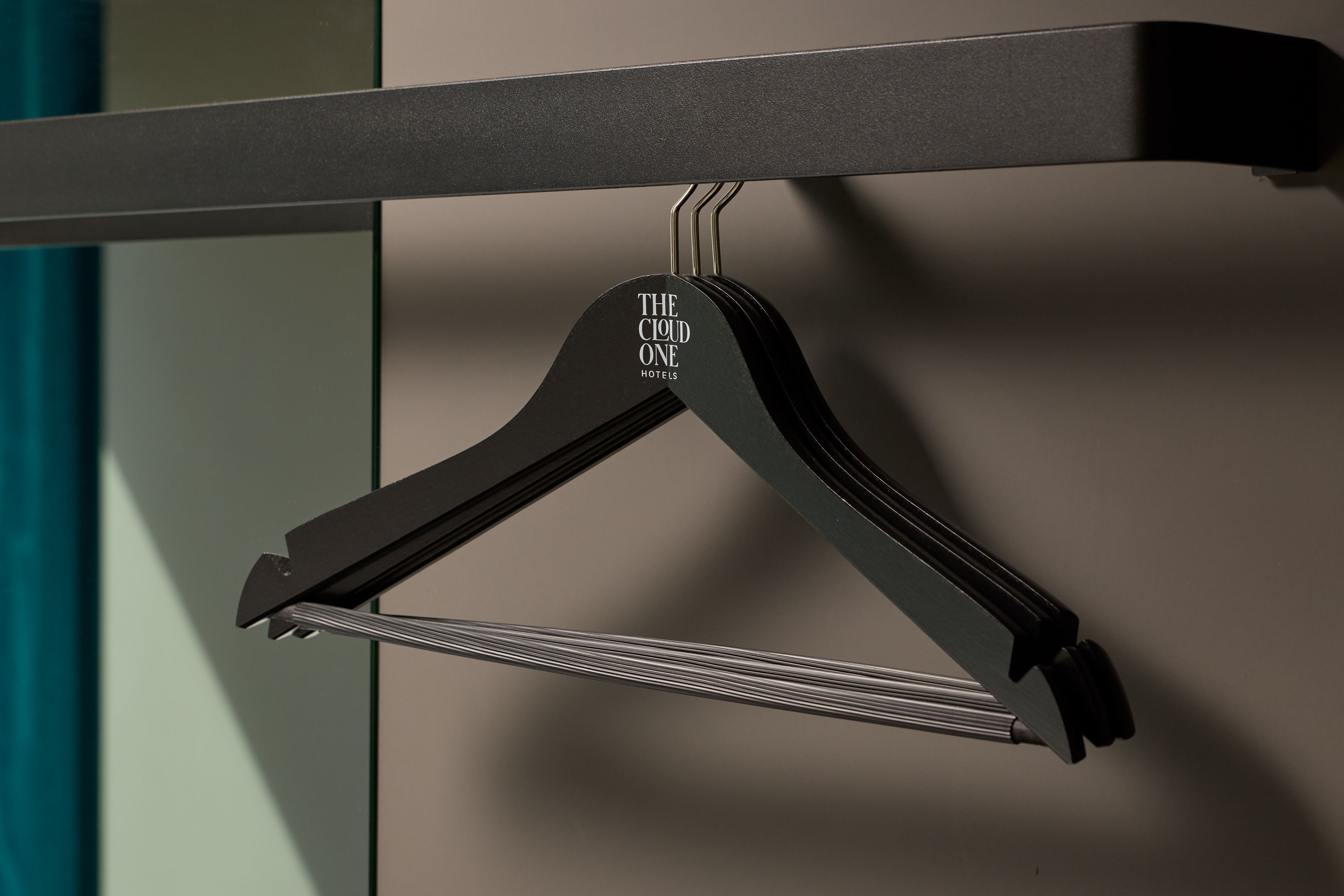 Schwarze Kleiderbügel aus Holz mit Hotelnamen „The Good One“ an einer Garderobenstange, in schlichtem, modernem Design und neutraler Beleuchtung.