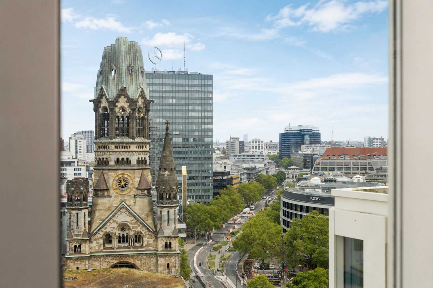 The Cloud One Berlin-Upper West Blick aus einem Fenster auf die Kaiser-Wilhelm-Gedächtniskirche in Berlin, umgeben von modernen Gebäuden und belebten Straßen mit Bäumen und Verkehr.