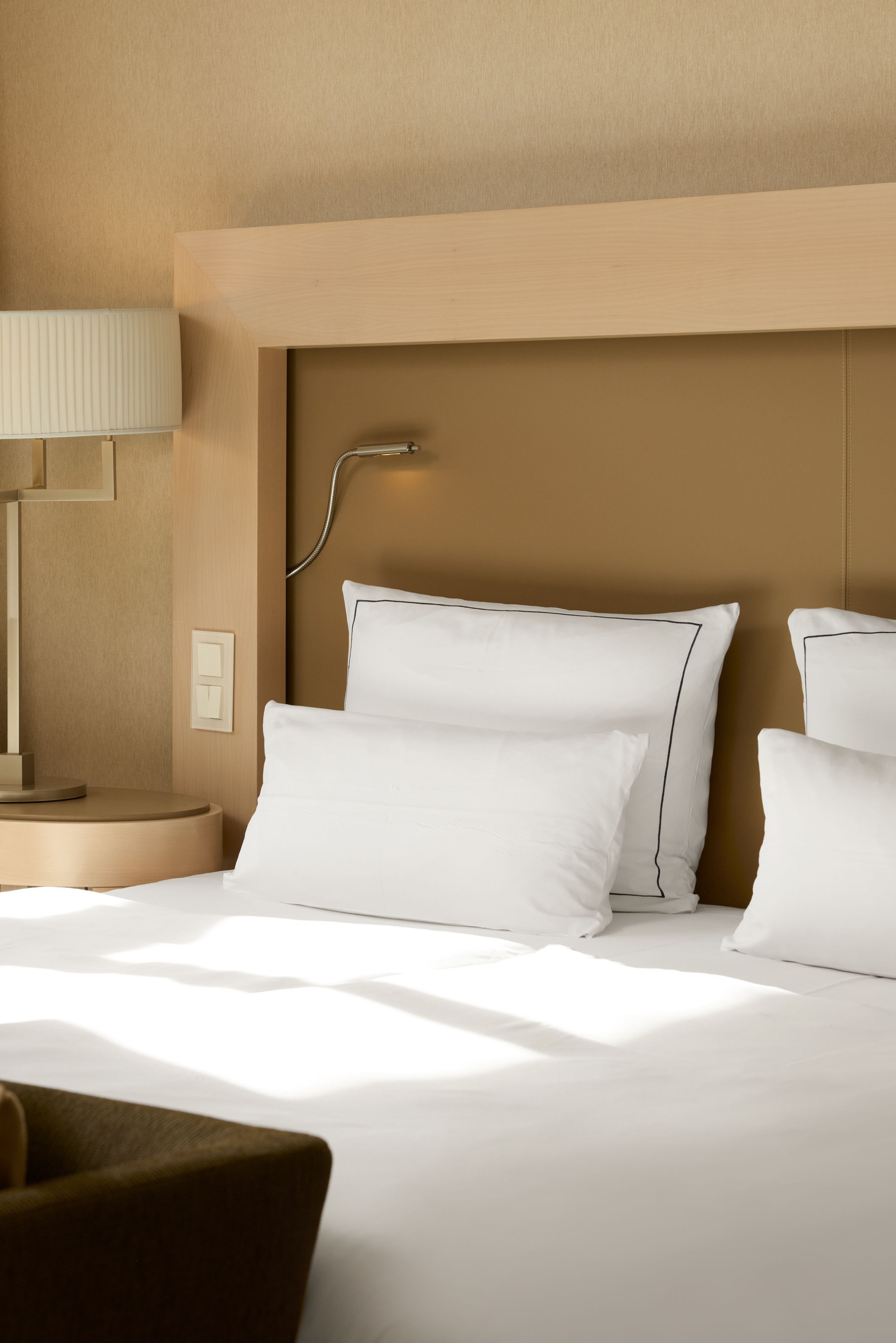 Schlicht gestaltetes Hotelzimmer mit weiß bezogenem Doppelbett, weichen Kissen und modernem Nachttisch mit Lampe. Helles, einladendes Ambiente fördert erholsamen Schlaf und Entspannung.