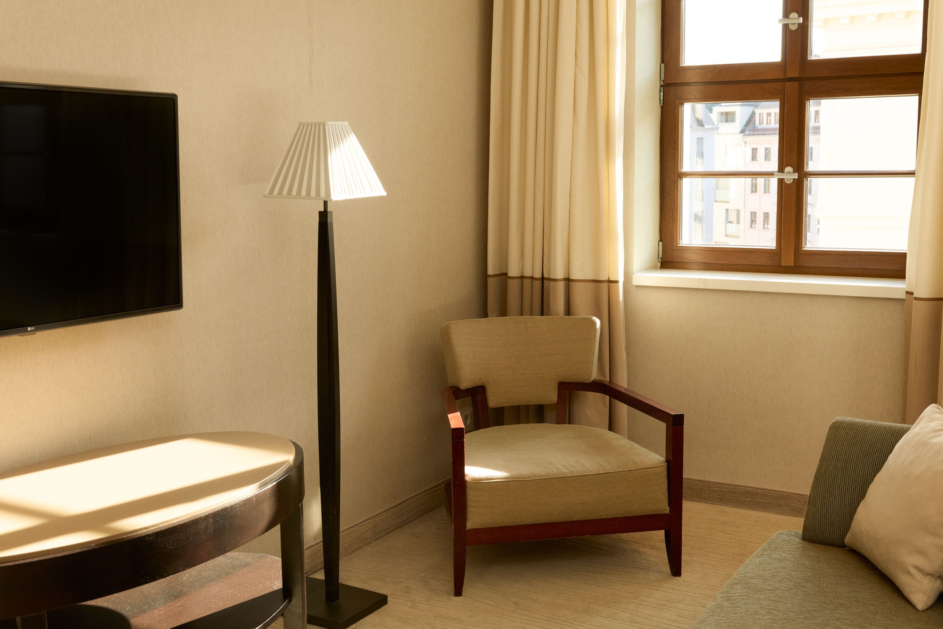 Helles, gemütliches Zimmer mit bequemen Sesseln, großem Fenster mit Ausblick und modernem Stehlampenlicht, ideal zum Entspannen.