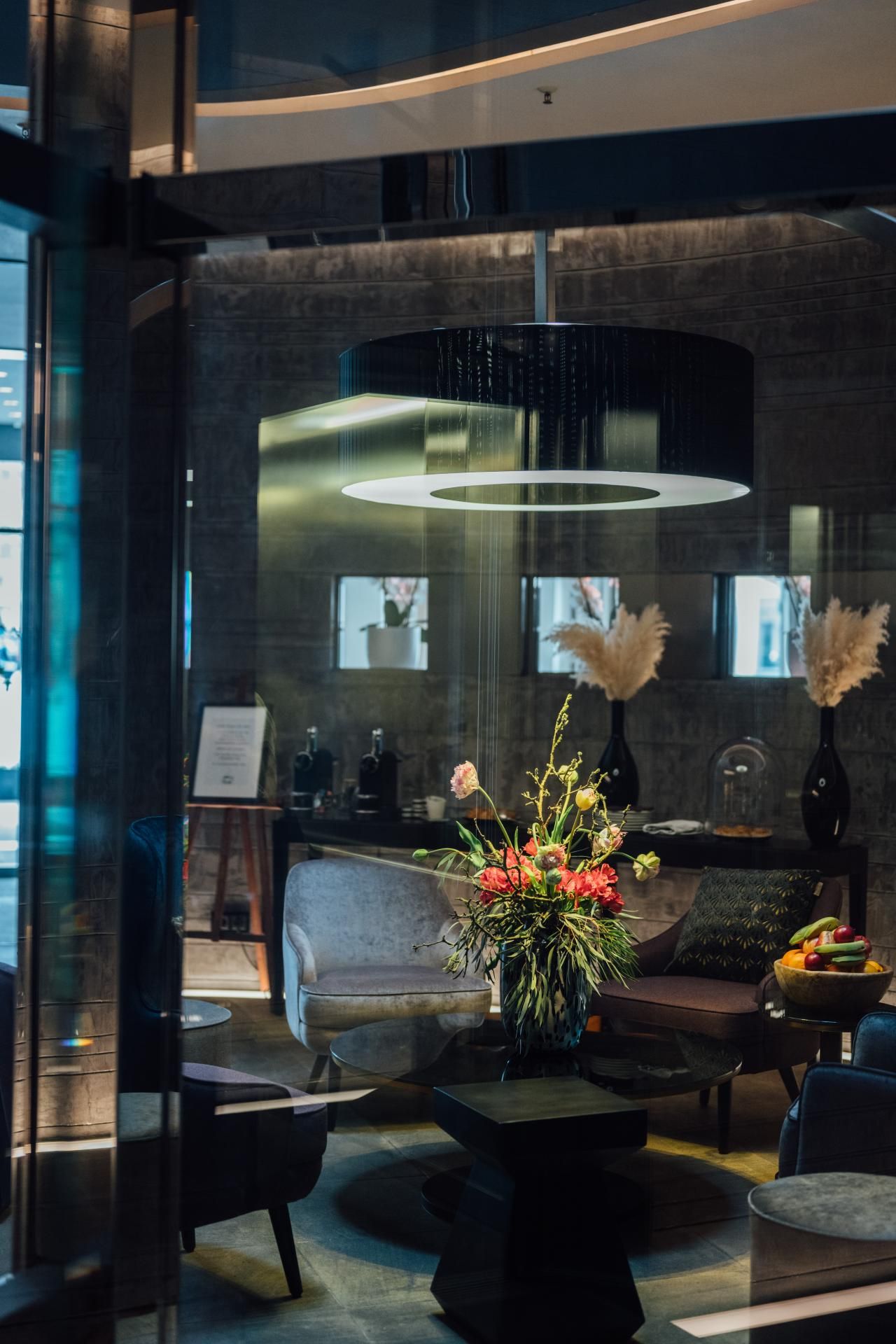 Elegantes, modernes Lounge-Ambiente mit gemütlicher Sitzgruppe, stilvoller Beleuchtung und einem zentral platzierten Blumenarrangement, das Wärme und Komfort ausstrahlt.