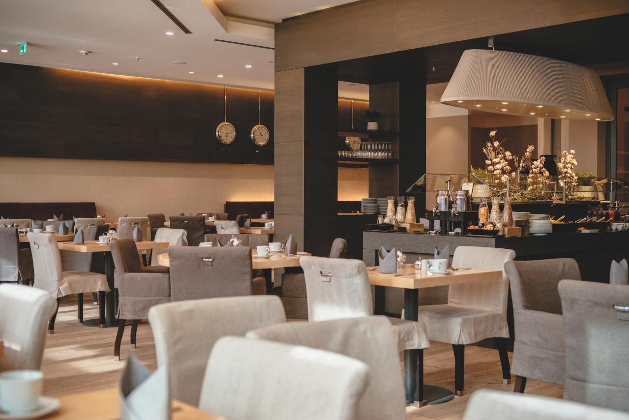 Modern eingerichteter Hotelrestaurant-Bereich mit gedeckten Tönen, bequemen Stühlen und gedeckten Holztischen. Freundliche Atmosphäre, ideal für entspannte Mahlzeiten in ruhigem, stilvollem Ambiente.