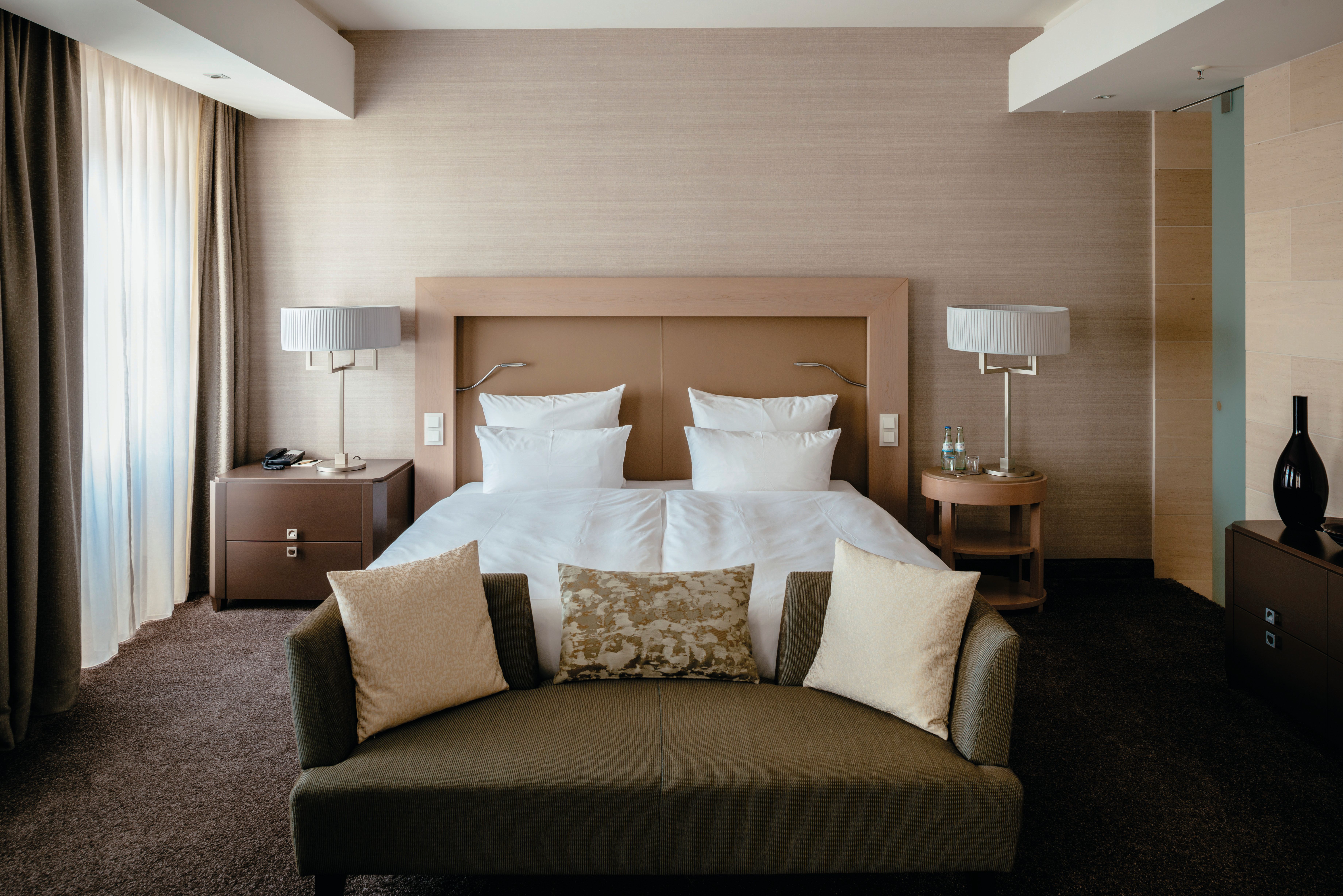 Modern eingerichtetes Hotelzimmer mit großem Doppelbett, weichen Kissen und gemütlicher Couch, sanfte Beleuchtung und neutralen Farben für entspannte Atmosphäre.