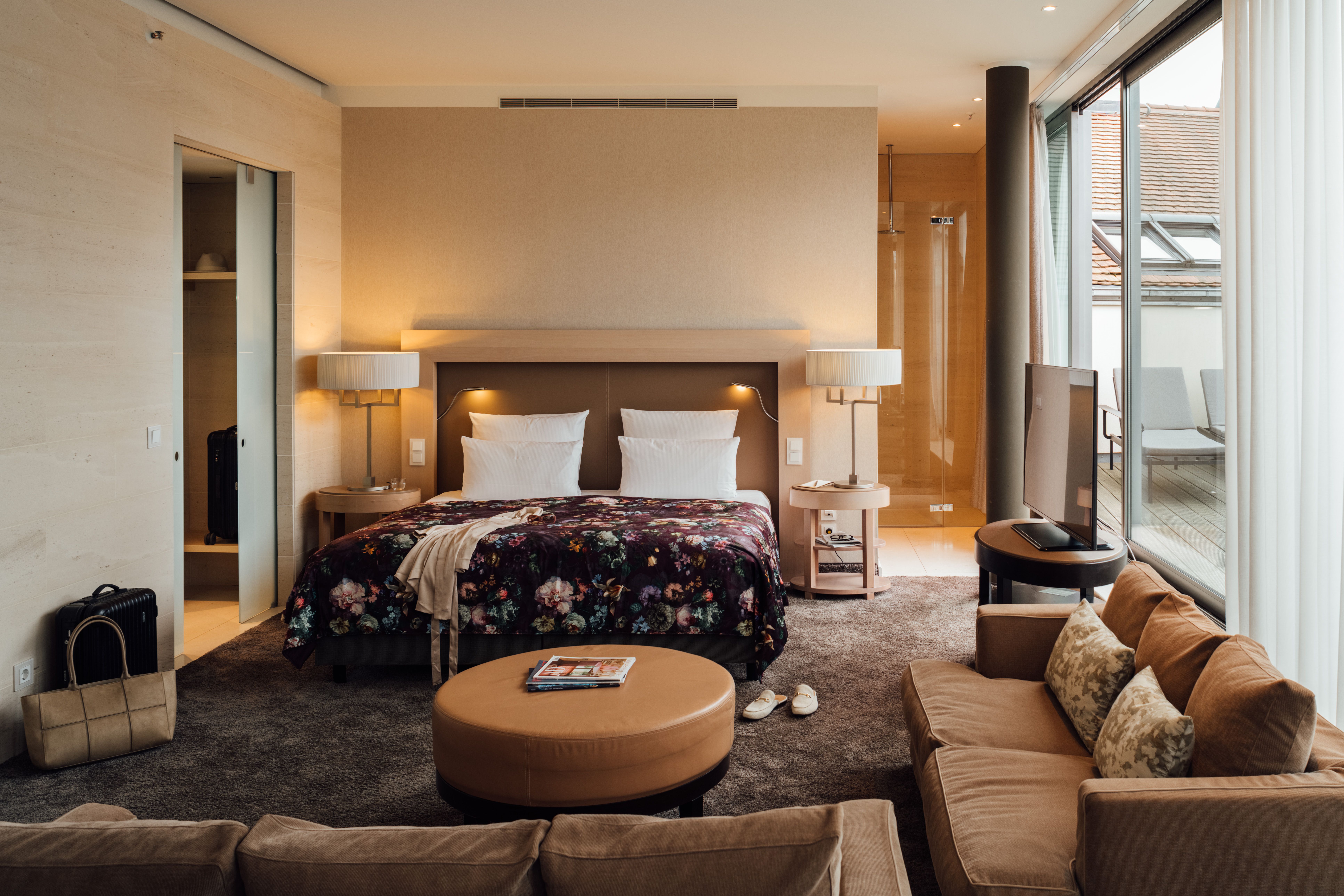 Modern eingerichtetes Hotelzimmer mit großem Doppelbett, gemütlichem Sofa, warmem Licht und Zugang zu einem Balkon mit Außenblick für entspannte Aufenthalte.