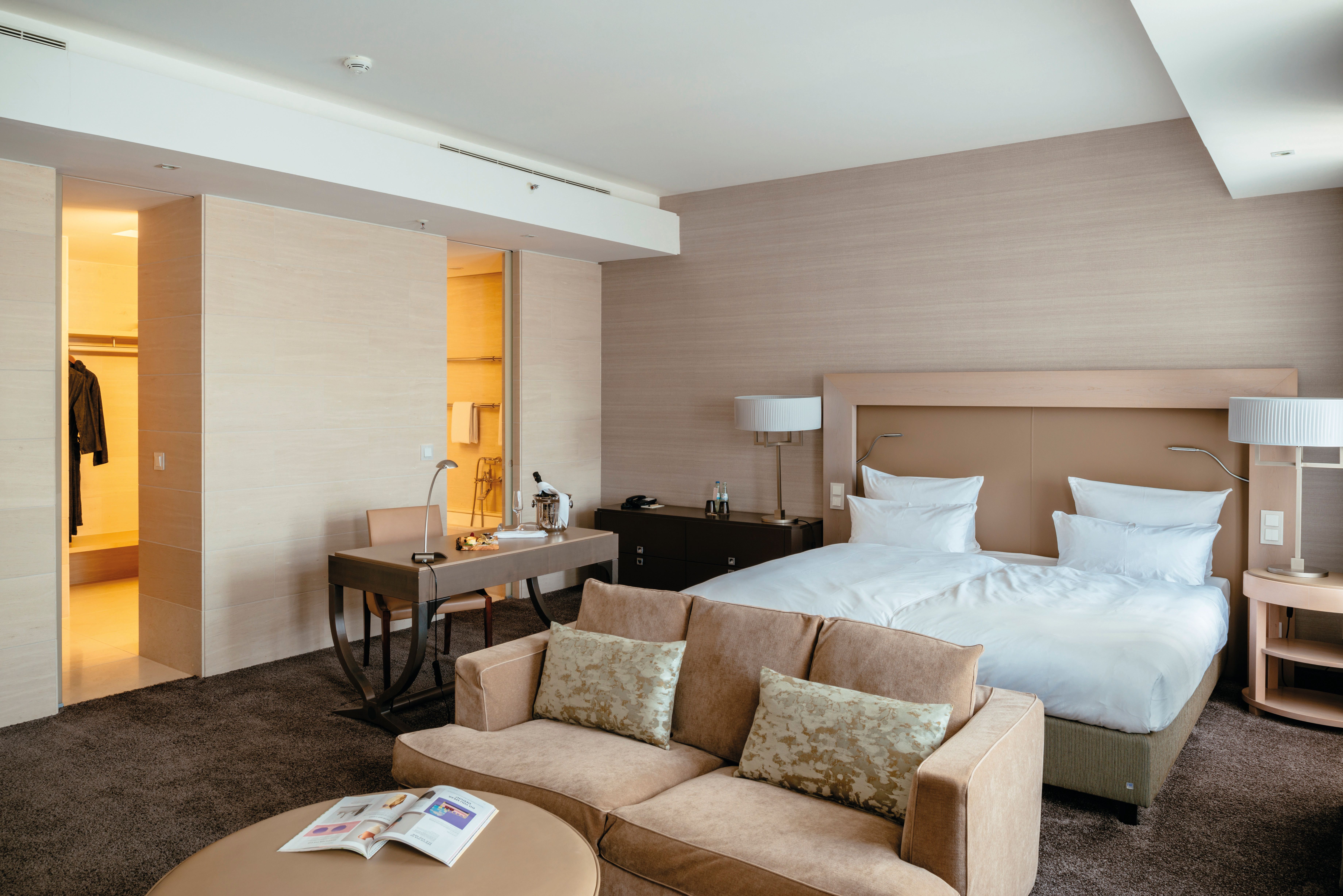 Modern eingerichtetes Hotelzimmer mit großem Doppelbett, gemütlichem Sofa, Schreibtisch und sanfter Beleuchtung, das eine entspannte und komfortable Atmosphäre bietet.