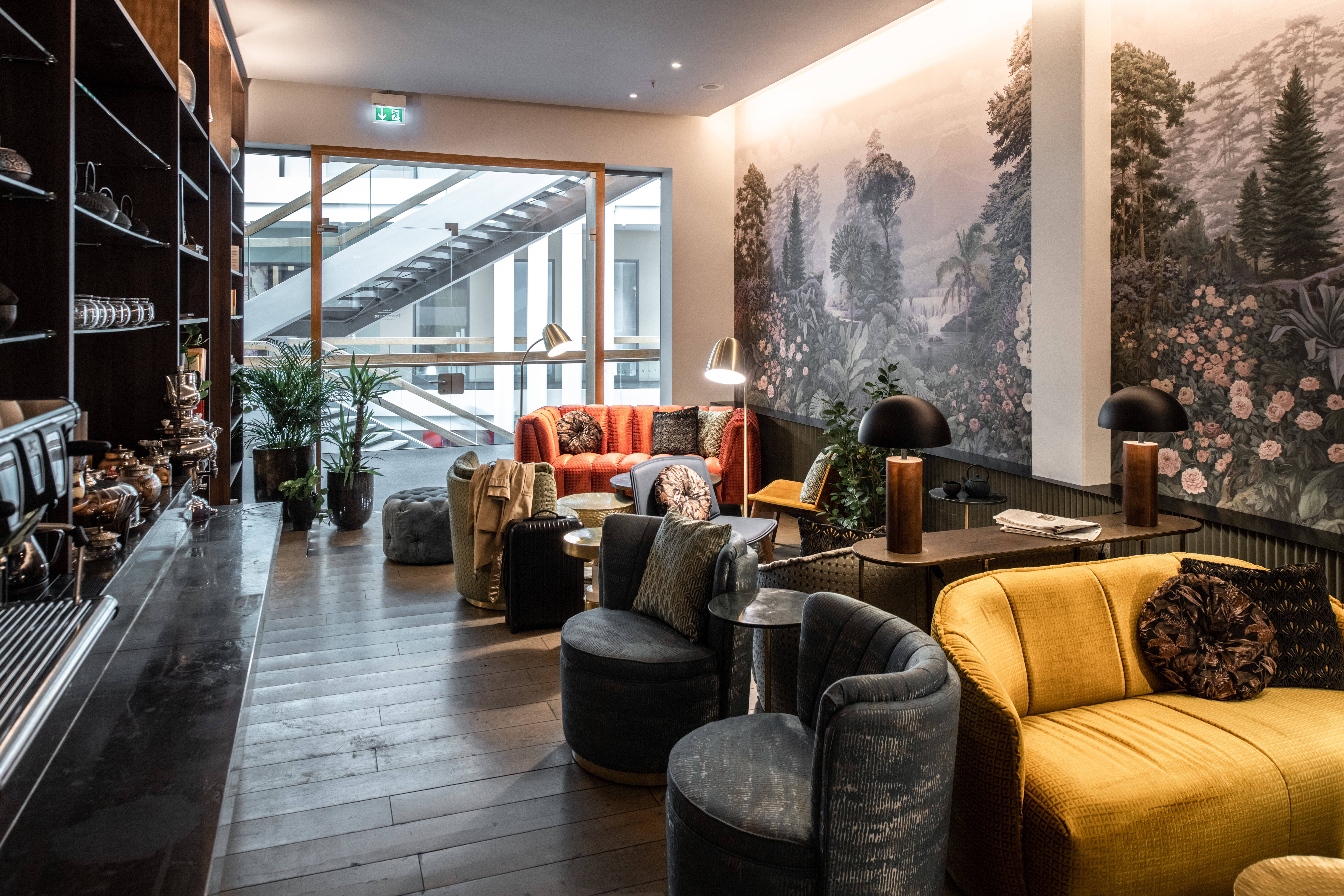 Gemütlicher Lounge-Bereich mit bequemen Sesseln und Sofas in warmen Farben, stimmungsvolle Beleuchtung und Wandbilder mit Naturmotiven, ideal zum Entspannen und Verweilen.