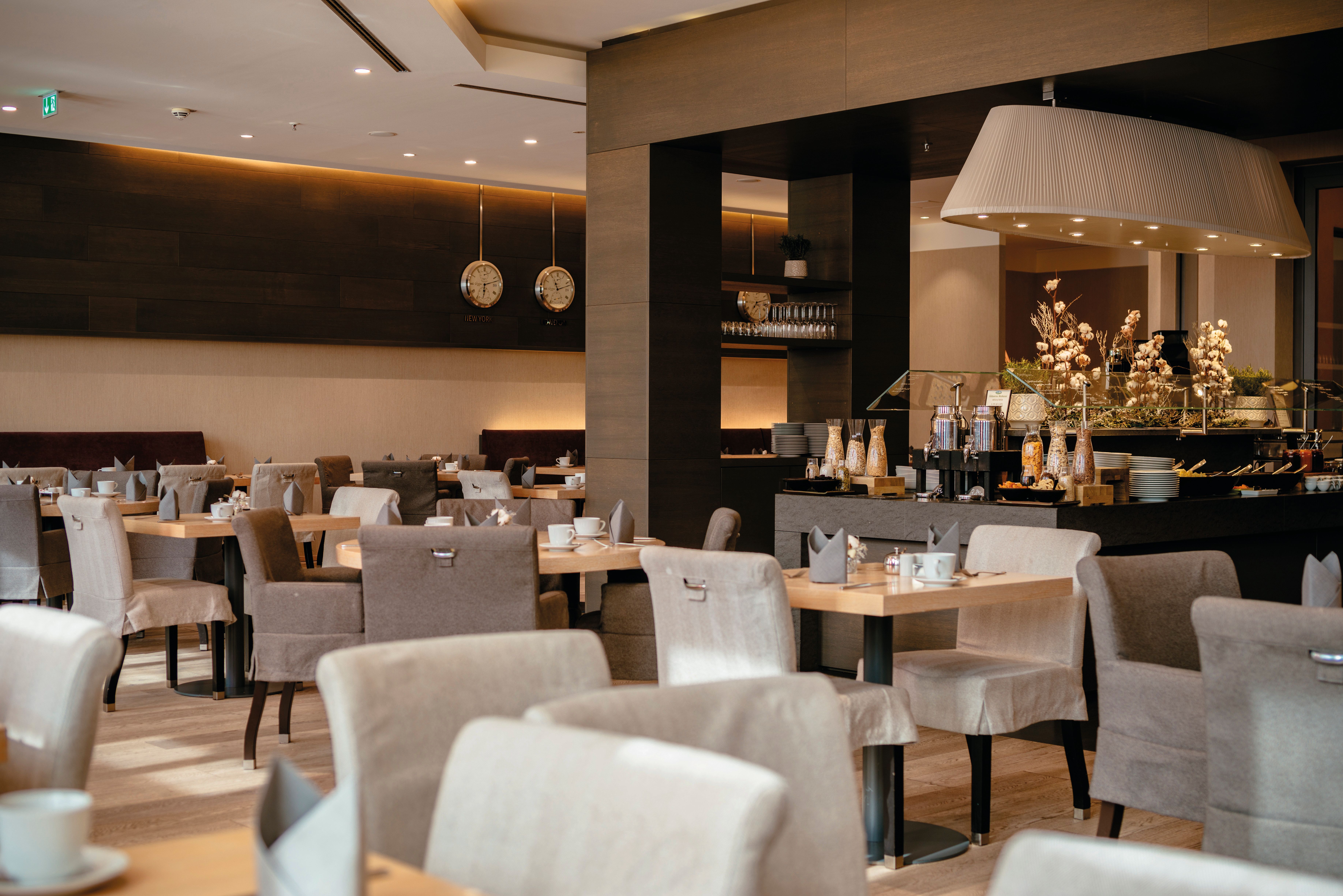 Modern eingerichteter Hotelrestaurantbereich mit gedeckten Tischen, bequemen Stühlen und warmer, einladender Beleuchtung für entspannte Mahlzeiten in elegantem Ambiente.