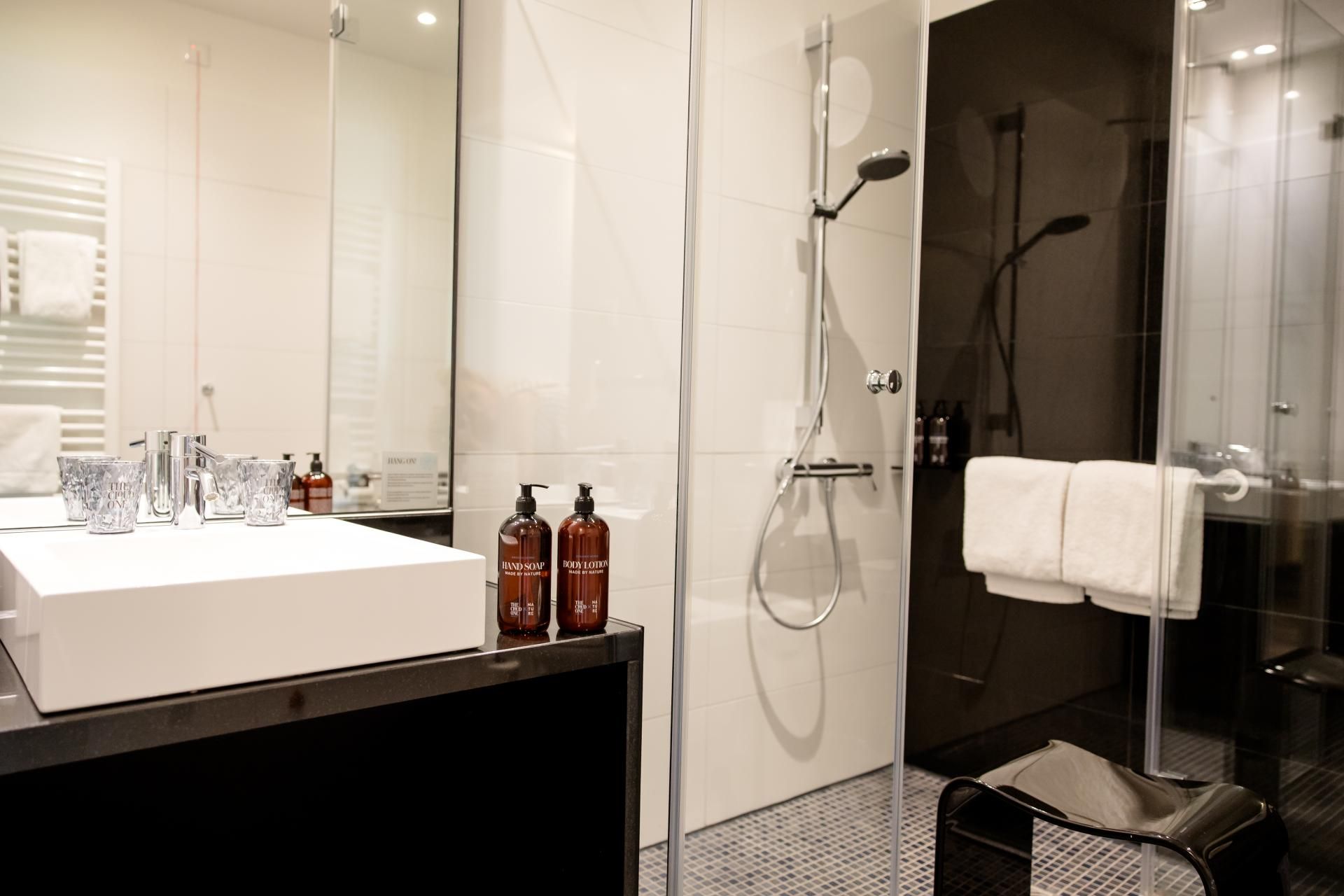 Moderne, helle Badezimmer mit großer Glasdusche, eingelassener Armatur und stilvollem Waschbecken. Handtücher und hochwertige Pflegeprodukte sorgen für Komfort und Entspannung. Cleanes, elegantes Design schafft Wohlfühlambiente.