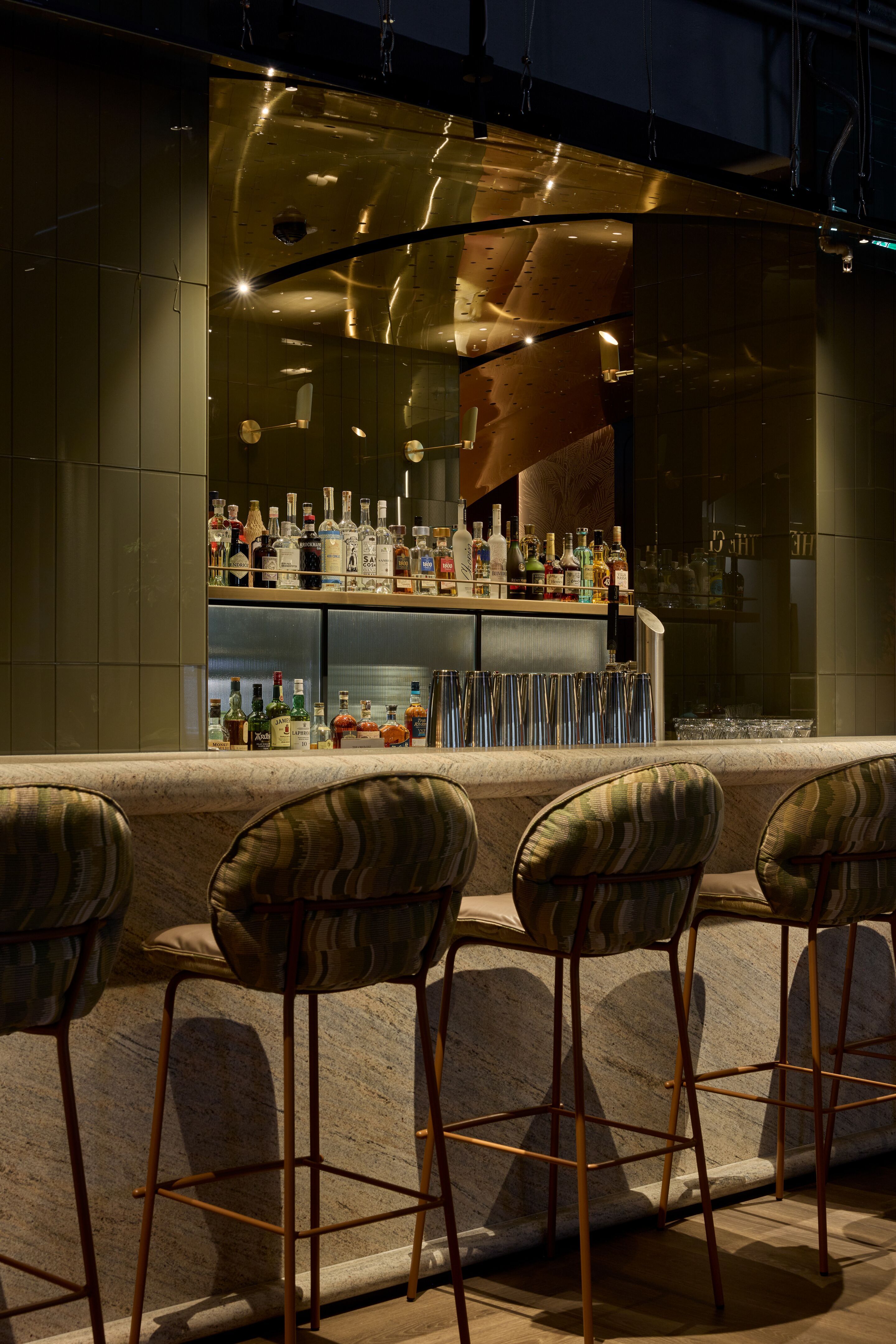 Designhotel Frankfurt Metropolitan The Cloud One Hotelbar mit gepolsterten Barhockern, beleuchteter Theke und gut sortiertem Regal mit Spirituosen, ideal für entspannte Abende und gesellige Momente.