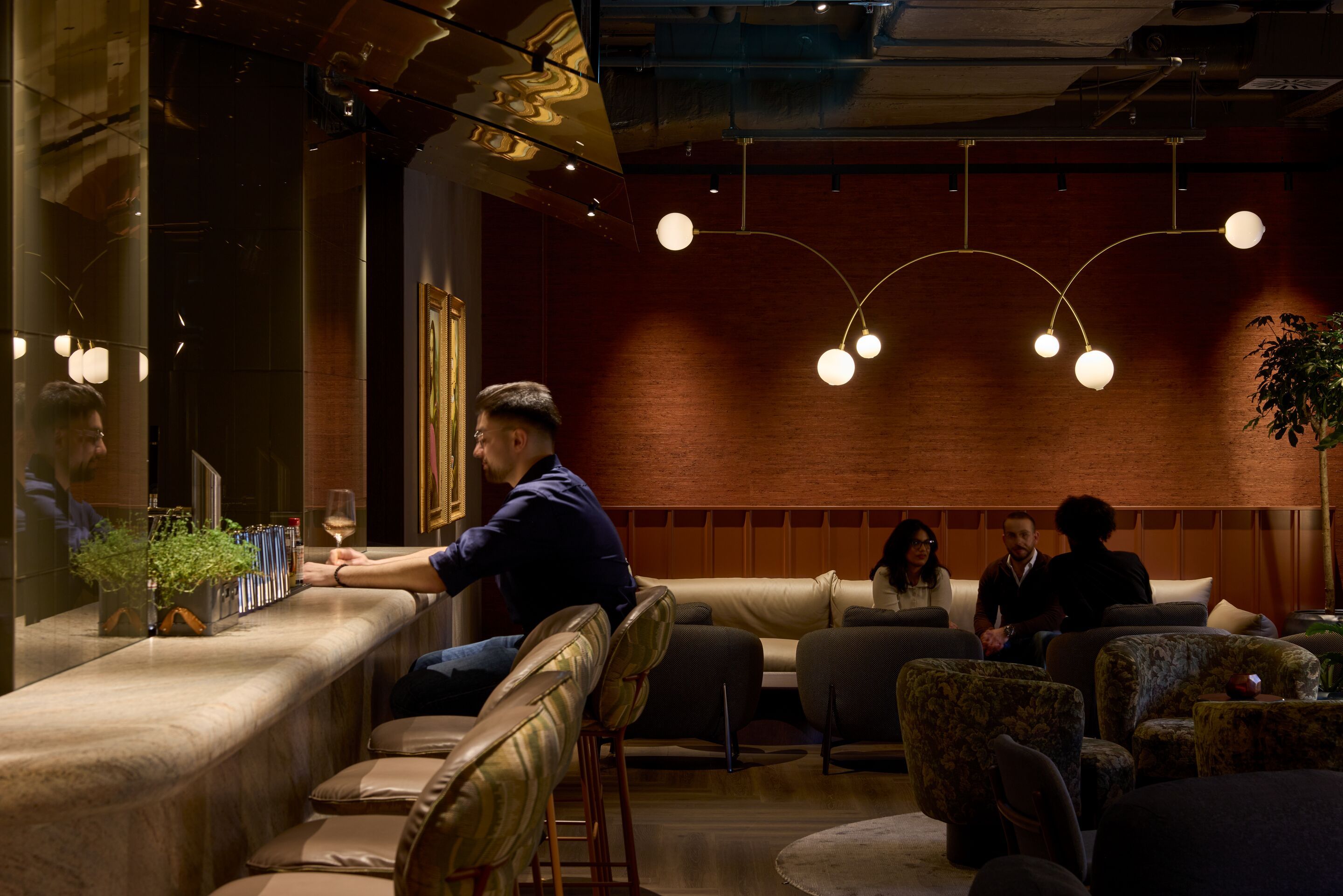 Hotel Frankfurt Metropolitan The Cloud One Lounge und Bar mit reduziertem Licht und Gäste sitzen entspannt an der Bar und auf bequemen Sofas, genießen Getränke und Gespräche in intimer Atmosphäre.