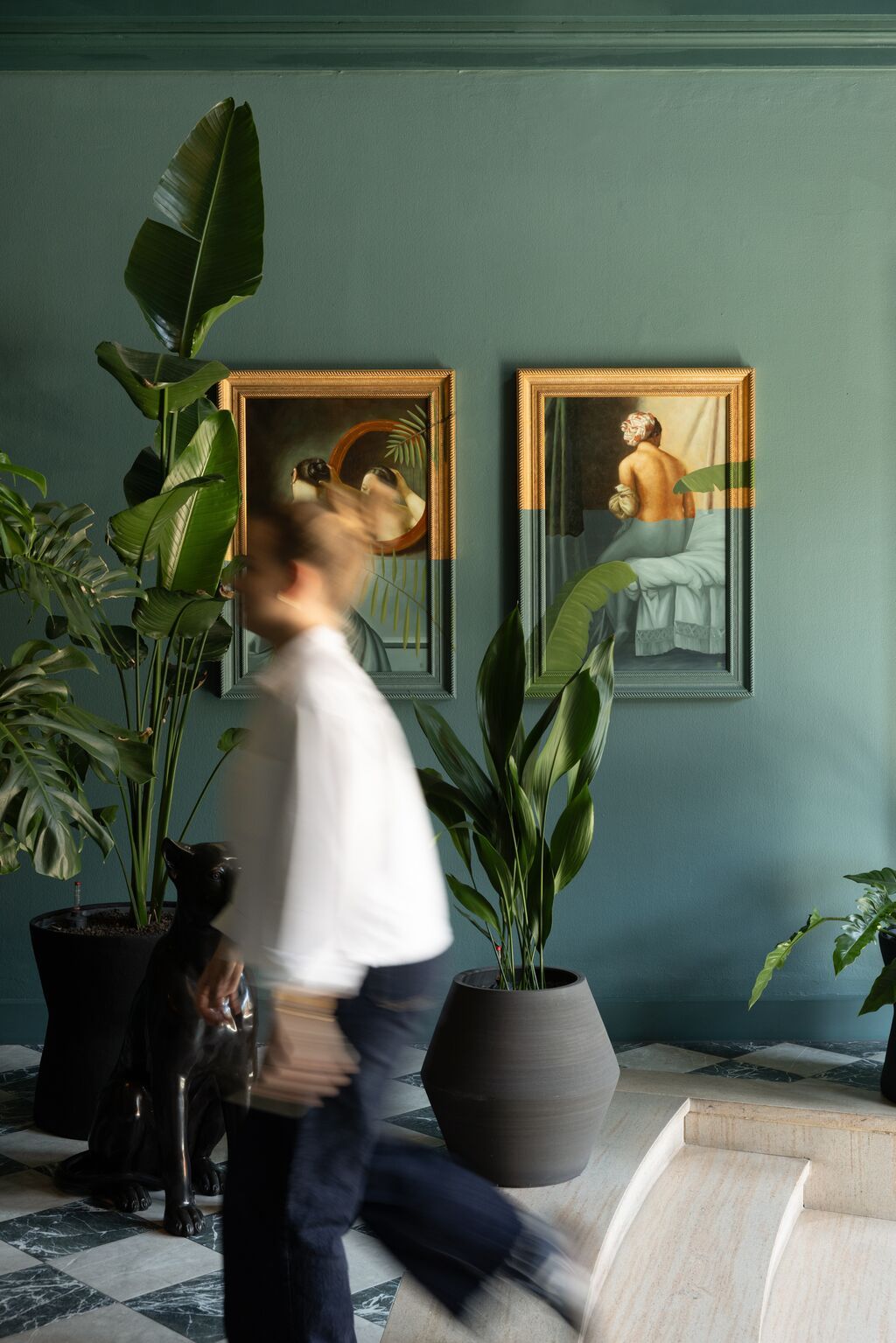 Hotel Frankfurt-Metropolitan The Cloud One Flur mit grünen Wänden, eleganten Pflanzen und stilvollen Kunstbildern, die eine entspannte und einladende Atmosphäre schaffen. Ein Gast geht vorbeigehend, was die lebendige Umgebung unterstreicht.