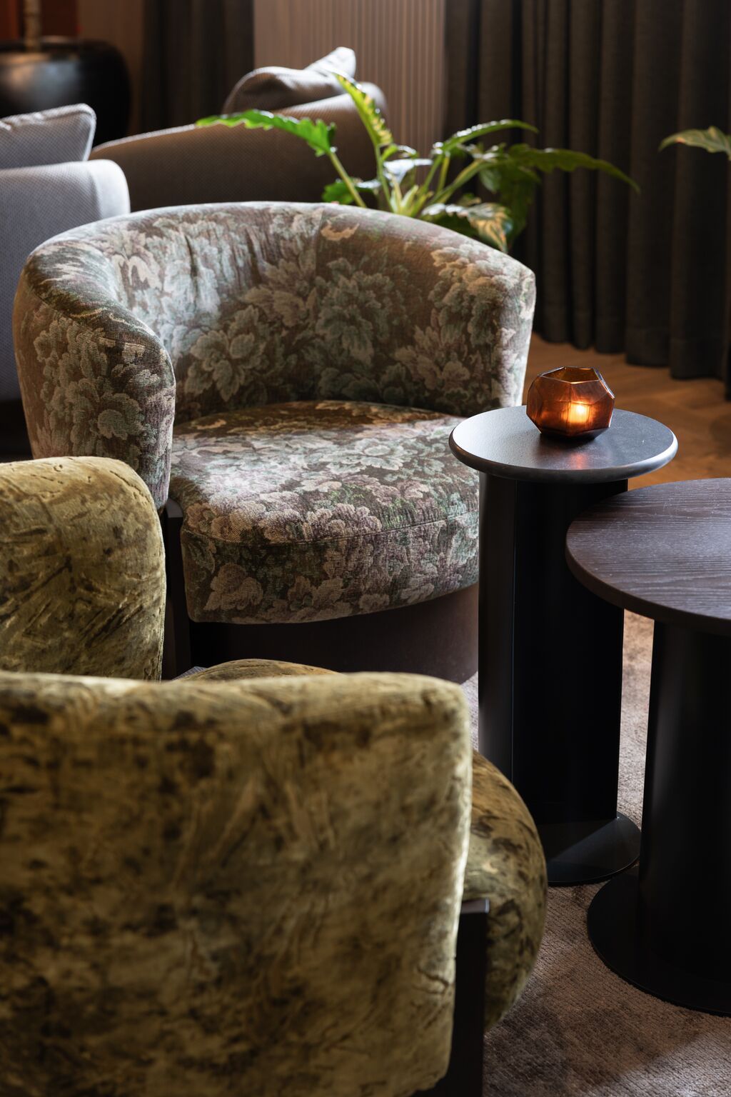 Hotel Frankfurt-Metropolitan The Cloud One gemütliche Sitzgruppe mit weichen, floral gemusterten Sesseln und dunklem Beistelltisch, dekoriert mit einer kleinen, warm leuchtenden Kerze.