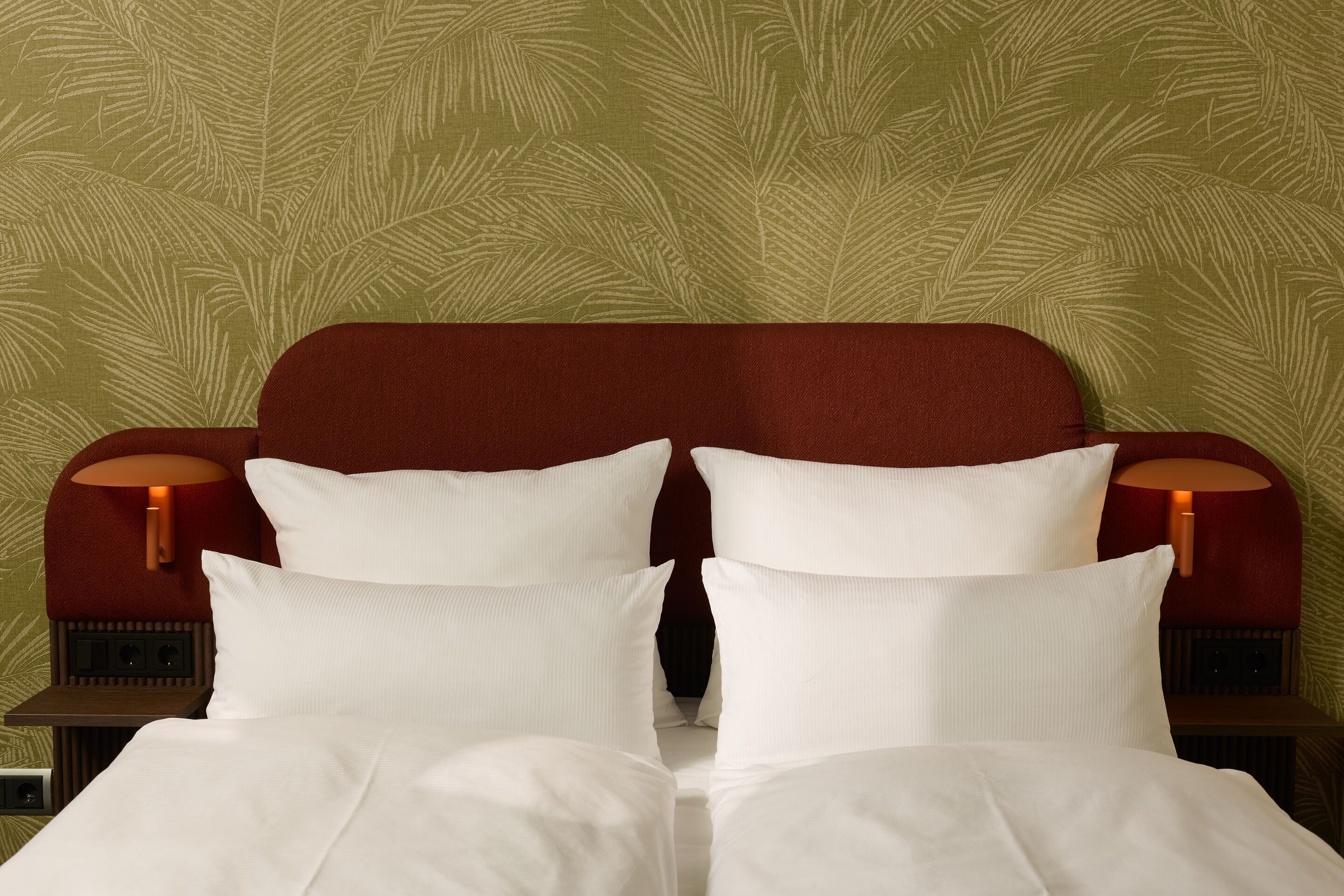 Hotel Frankfurt-Metropolitan The Cloud One helles Hotelzimmer mit Doppelbett, weichen weißen Kissen und sauberer Bettwäsche. Warme, gemütliche Atmosphäre durch dunkelrotes Kopfteil und dezente grüne Wandgestaltung.