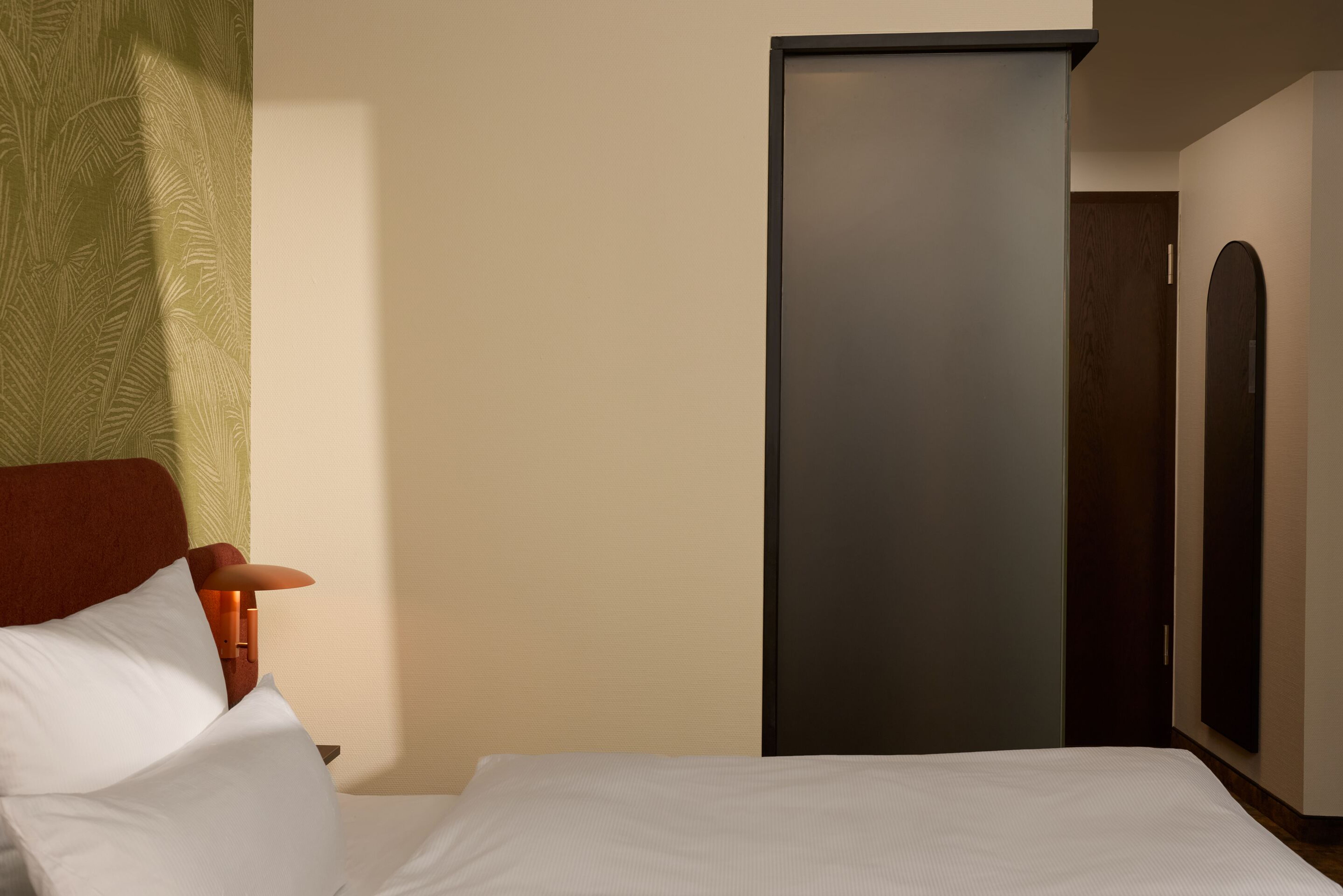 Hell eingerichtetes Hotelzimmer mit großem, weiß bezogenem Bett, stilvoller Holzlampe und ruhiger, einladender Atmosphäre. Hell eingerichtetes Hotelzimmer mit großem, weiß bezogenem Bett, stilvoller Holzlampe und ruhiger, einladender Atmosphäre.