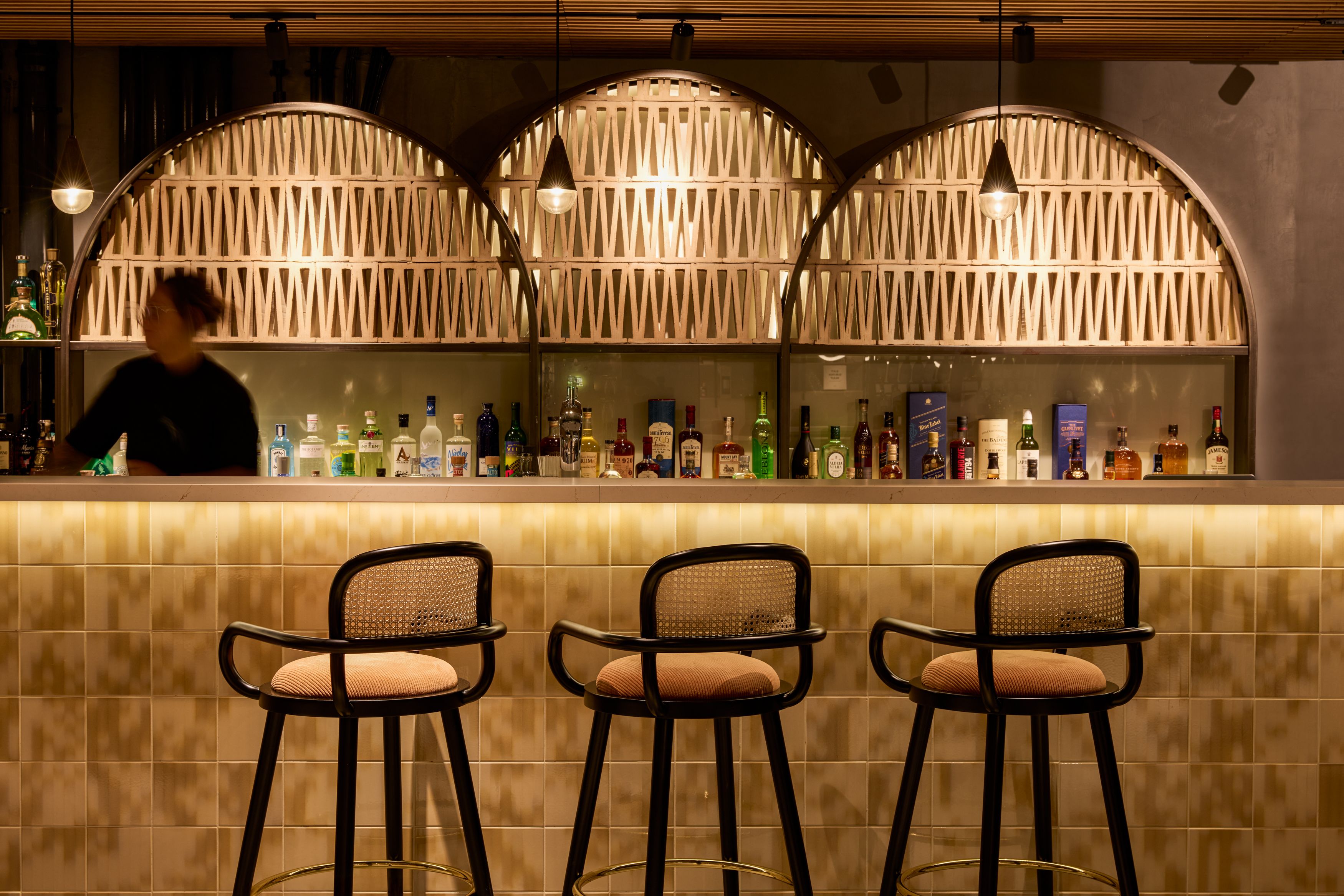 Designhotel Lissabon The Cloud One Bar mit stilvoll beleuchtetem Tresen und drei Barhockern, im Hintergrund eine großzügige Auswahl an Spirituosen.