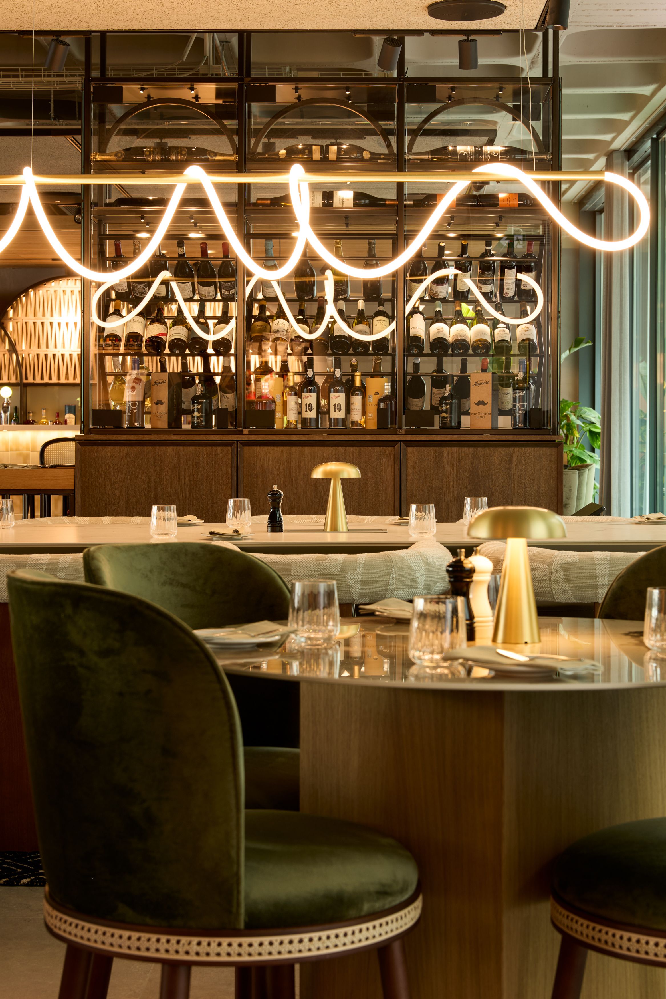 Hotel Lissabon The Cloud One Bar mit modernen, geschwungenen Deckenleuchten, grünen Samtstühlen und elegant gedeckten Tischen.