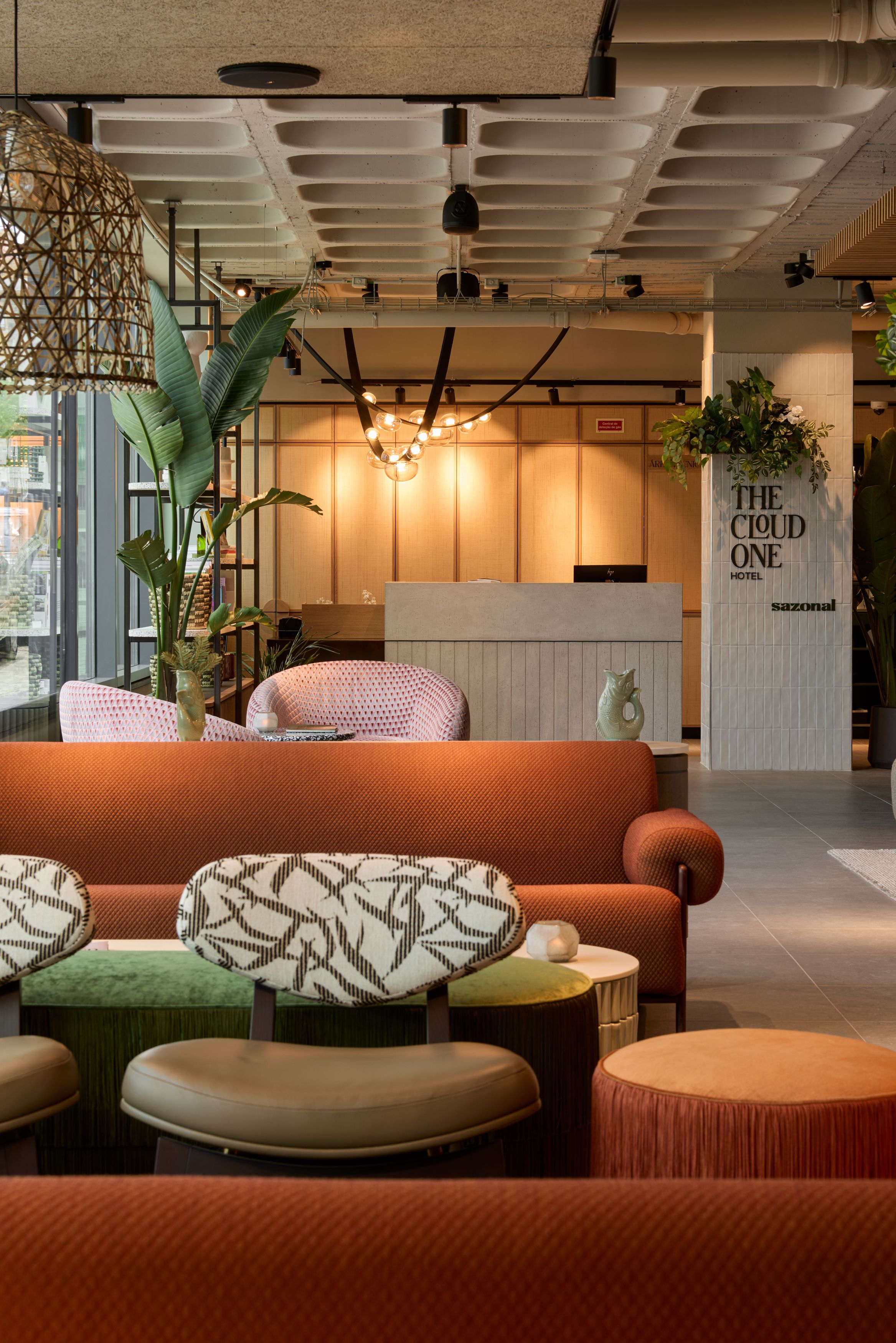 Hotel Lissabon The Cloud One Rezeption und Lounge mit Sitzmöglichkeiten in warmen Farben, Pflanzen und dezenter Beleuchtung. Empfangstresen im Hintergrund mit hellen Wänden und stilvollem Design.