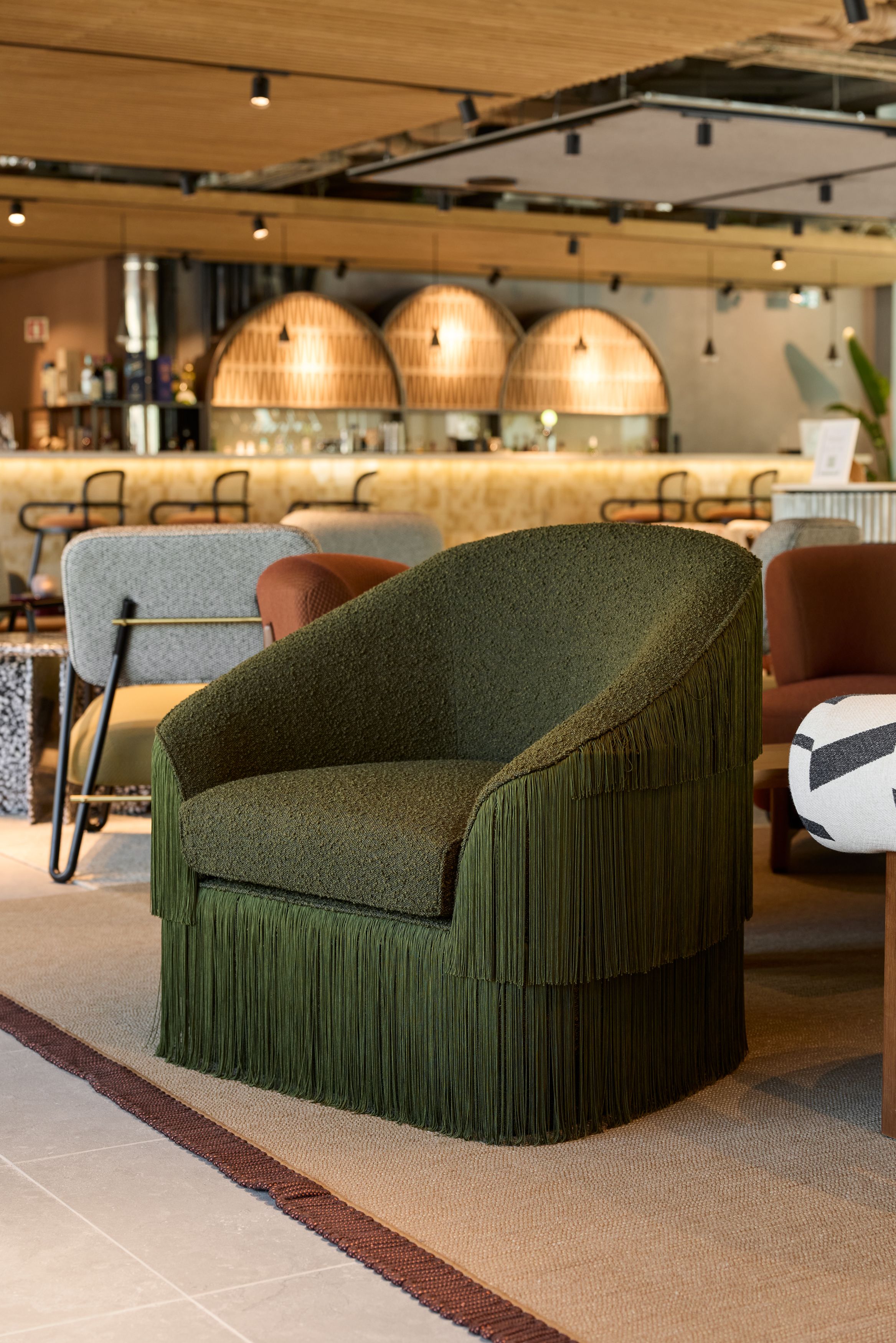 Hotel Lissabon The Cloud One dunkelgrüner Sessel mit dekorativem Fransenbesatz in einer stilvoll eingerichteten Hotel-Lounge mit warmem Licht und Bar im Hintergrund.