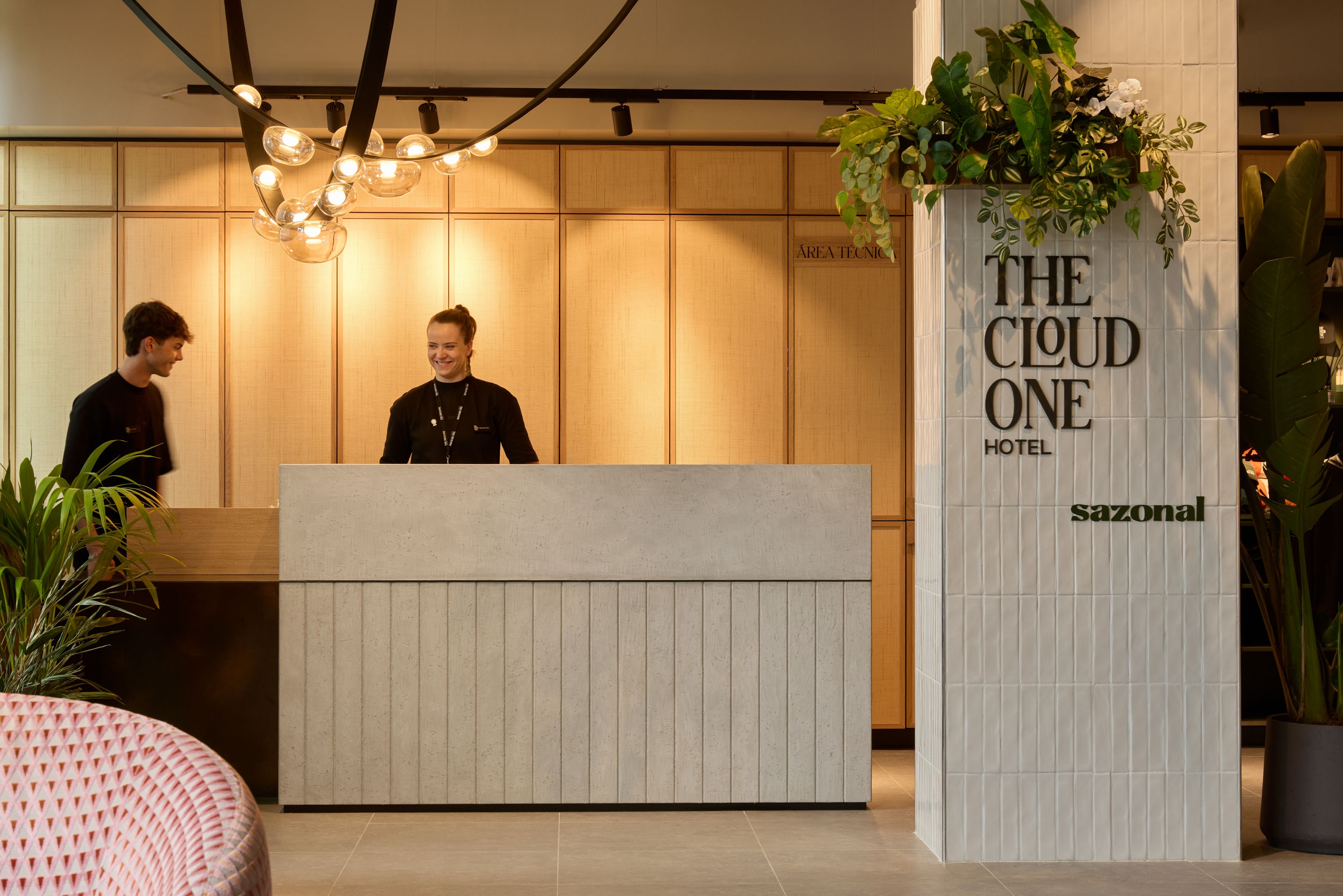 Designhotel Lissabon The Cloud One Rezeption mit zwei Mitarbeitenden. Die Einrichtung wirkt modern und einladend, mit warmen Holztönen und grünen Pflanzen für eine entspannte Atmosphäre.