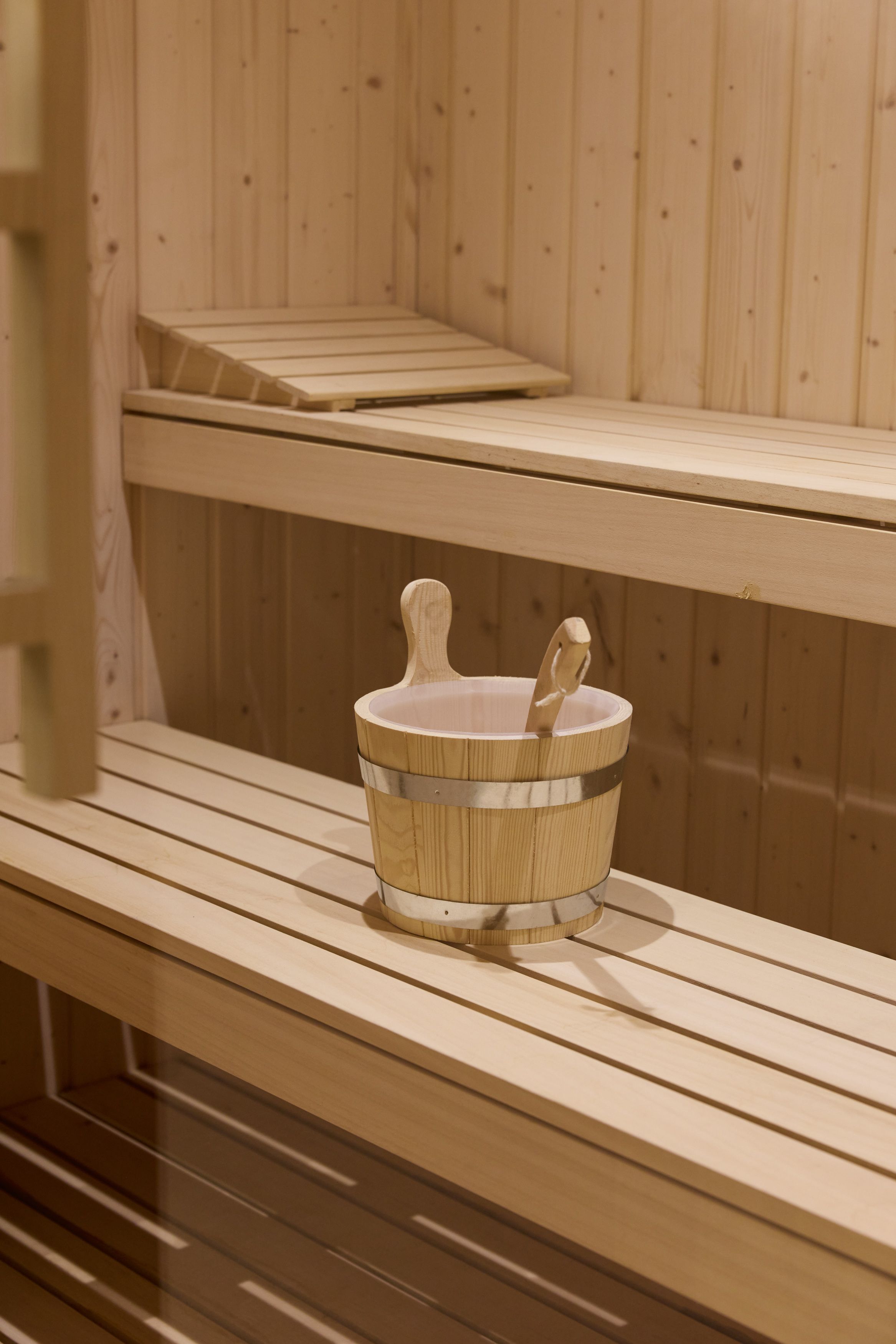 Hotel Lissabon The Cloud One Innenansicht einer holzverkleideten Sauna mit zwei mehrstufigen Sitzbänken und einem Wassereimer mit Schöpflöffel.