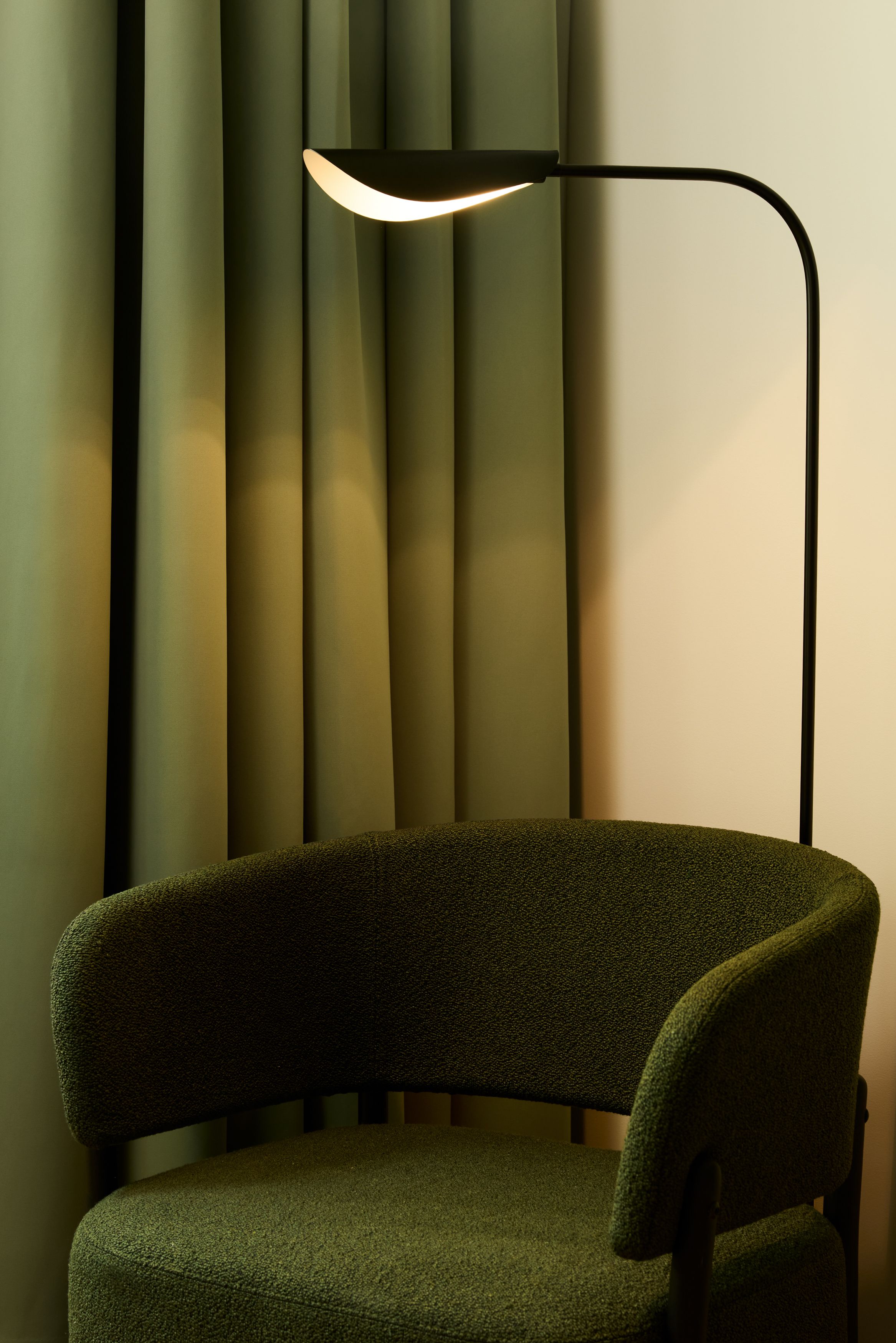 Hotel Lissabon The Cloud One dunkelgrüner Sessel vor geschlossenen grünlichen Vorhängen, daneben eine elegante, gebogene Stehlampe mit warmem, indirektem Licht.