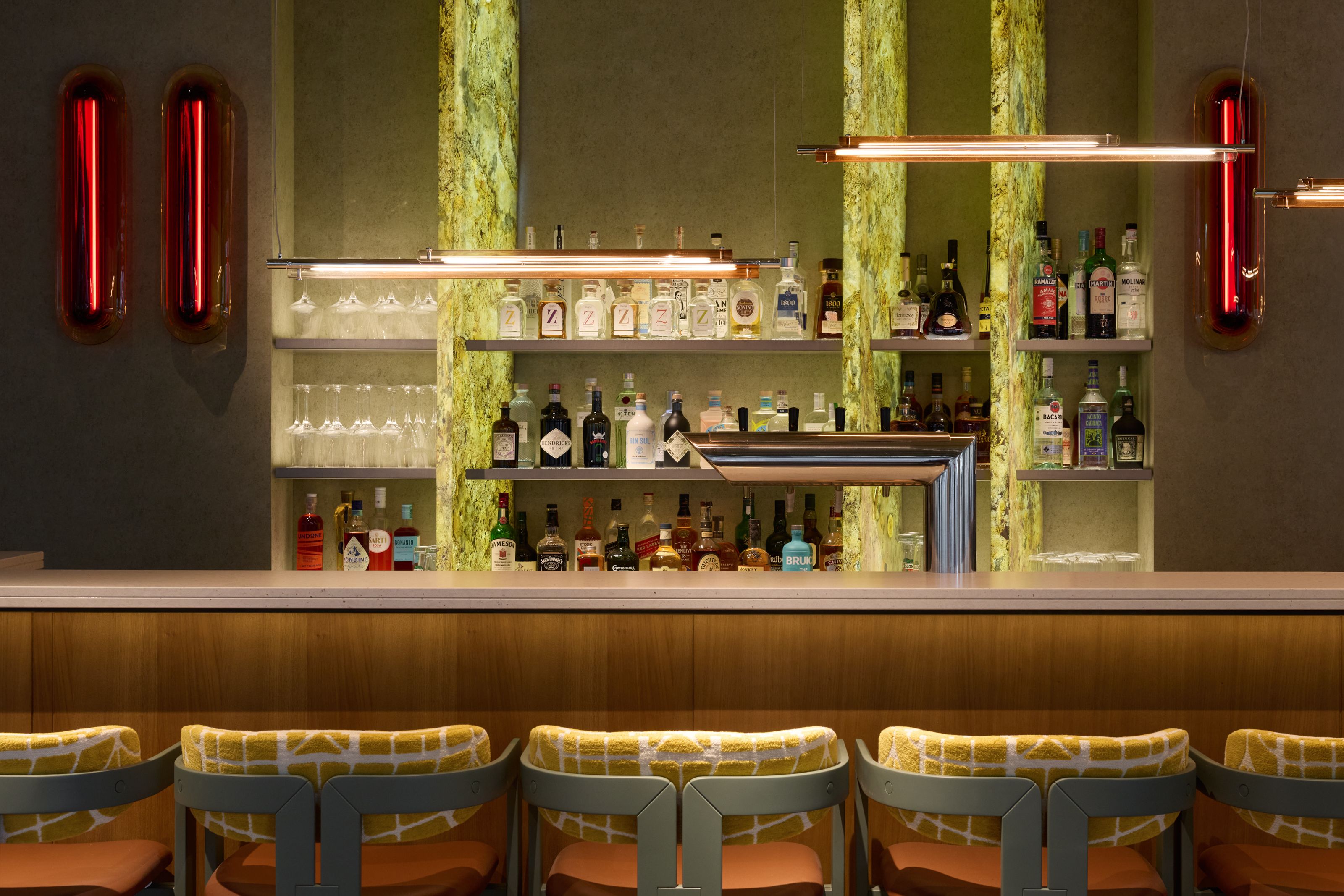 Moderne Hotelbar mit eleganter Beleuchtung, gut sortierten Spirituosenregalen und bequemen, gepolsterten Barhockern in warmem Ambiente für entspannte Abende und gesellige Momente.