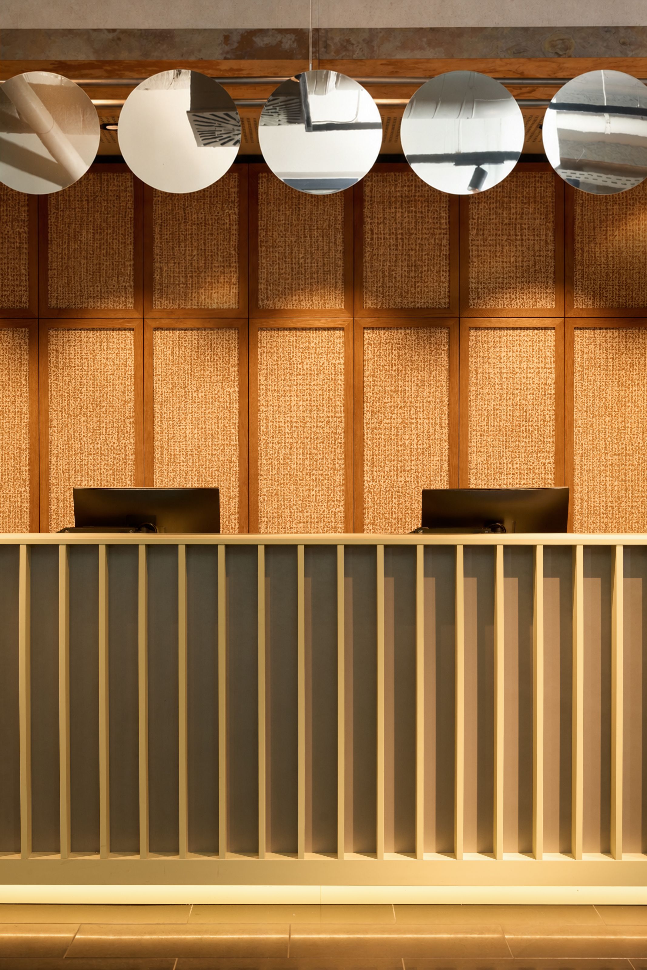 Rezeption mit modern gestaltetem Tresen vor einer Wand mit Textur und fünf spiegelnden, runden Dekorationen an der Decke, die den Raum elegant und einladend wirken lassen.