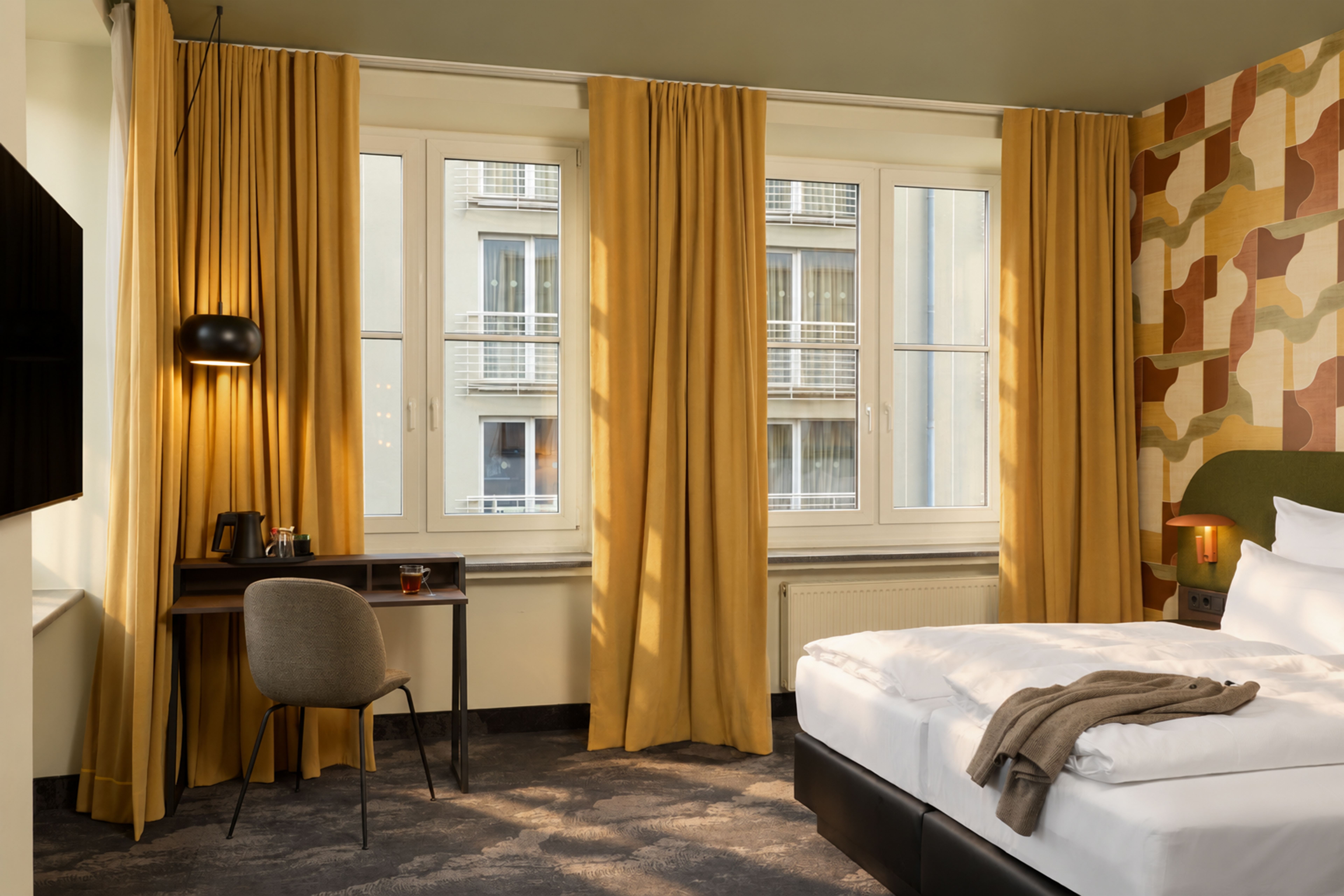 Helles Hotelzimmer mit großem Fenster, senfgelben Vorhängen, modernem Schreibtisch, gemütlichem Bett und dekorativer Wand. Ruhige, einladende Atmosphäre. Helles Hotelzimmer mit großem Fenster, senfgelben Vorhängen, modernem Schreibtisch, gemütlichem Bett und dekorativer Wand. Ruhige, einladende Atmosphäre.