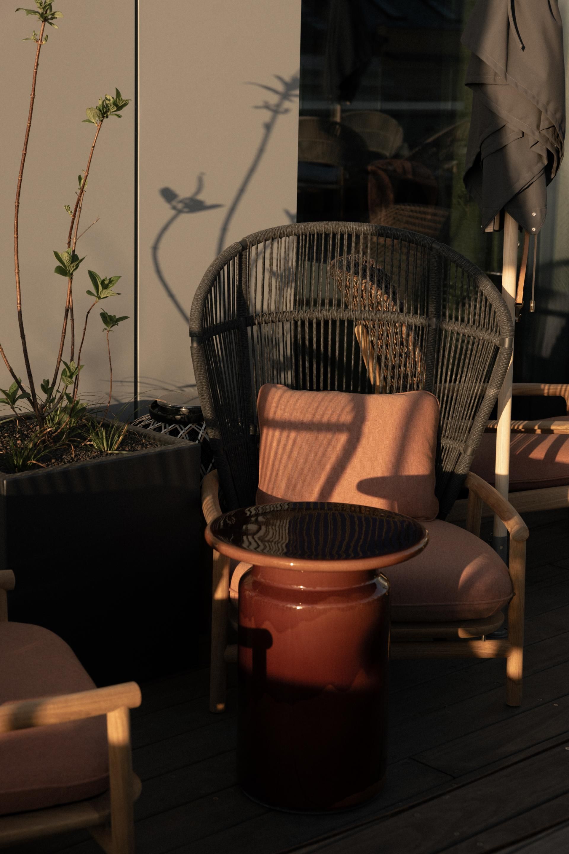 Gemütliche Terrasse mit einem modernen Korbsessel und kleinem Tisch, umgeben von Pflanzen. Sanftes, warmes Licht schafft eine entspannte Atmosphäre für Erholung im Freien.