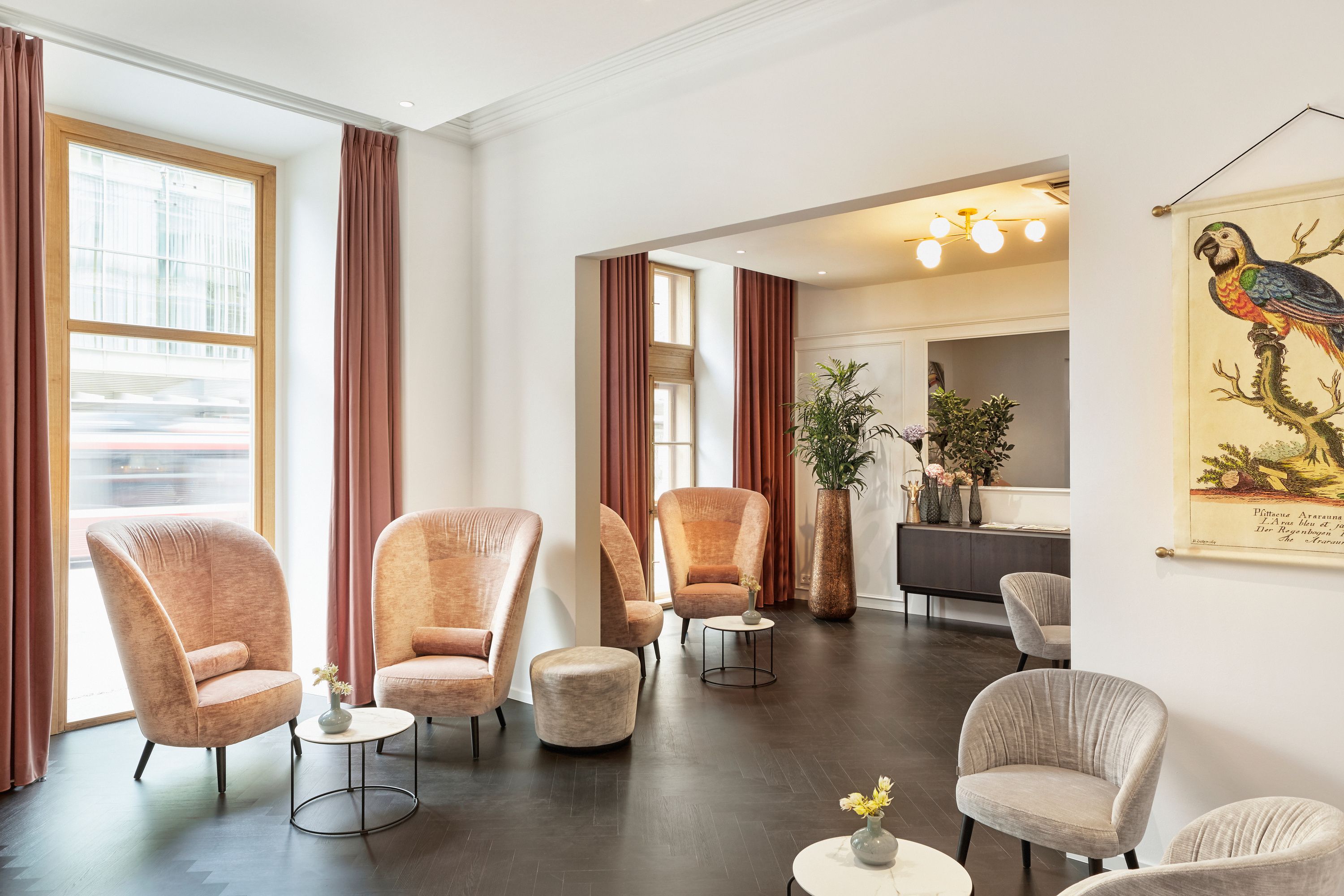 Helle, stilvoll eingerichtete Lounge mit bequemen Sesseln, kleinen Tischen und großen Fenstern, die viel Tageslicht bieten. Dezente Dekoration und Pflanzen schaffen eine einladende Atmosphäre zum Entspannen und Verweilen.