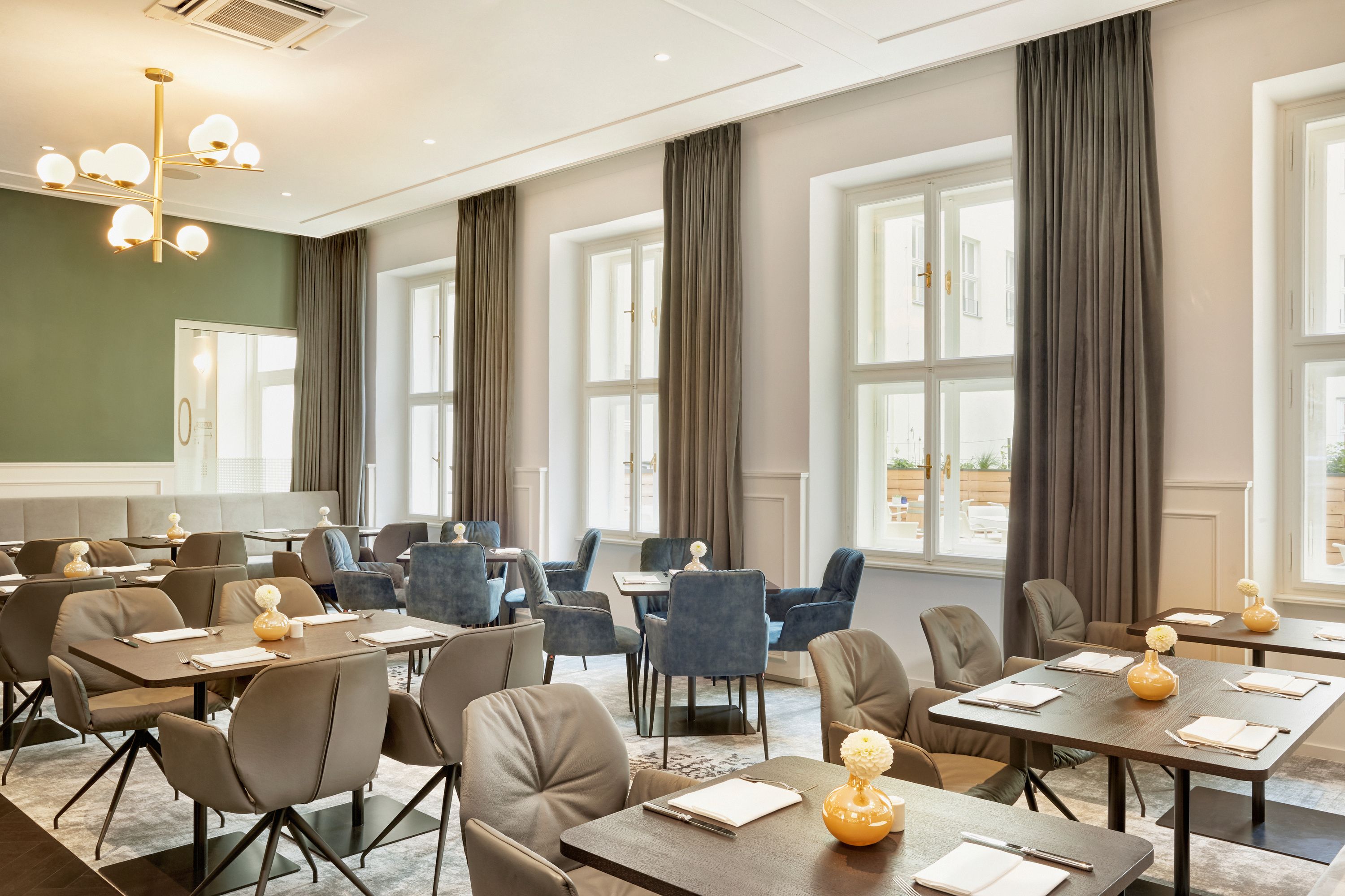 Helles, stilvoll eingerichtetes Restaurant mit gedeckten Tischen, bequemen Sesseln und großen Fenstern, die viel Tageslicht in den Raum lassen. Moderne Beleuchtung und ruhige Farbtöne schaffen eine einladende Atmosphäre zum entspannten Speisen.