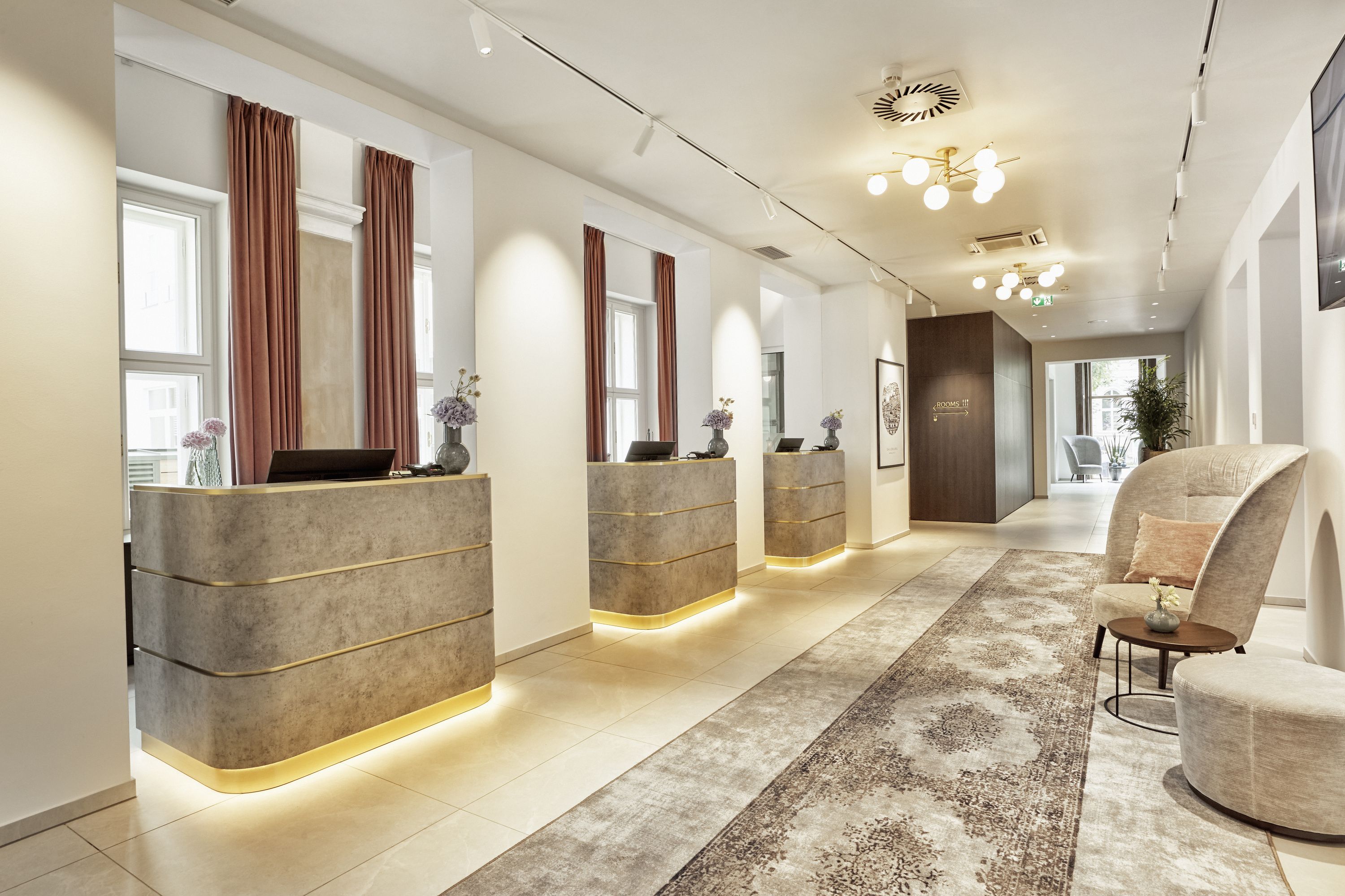 Moderne Hotelrezeption mit drei beleuchteten Empfangstresen, heller Atmosphäre und gemütlichem Sitzbereich, der Gästen einen einladenden ersten Eindruck vermittelt.