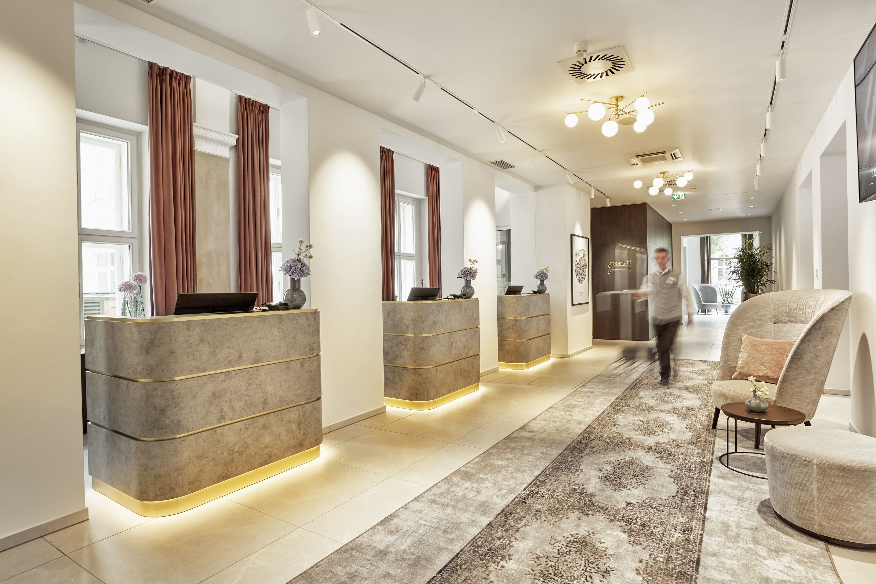 Heller, moderner Empfangsbereich mit stilvollen Tresen, weichen Teppichen und gemütlicher Sitzgelegenheit, freundlich beleuchtet und einladend gestaltet für einen angenehmen Check-in.