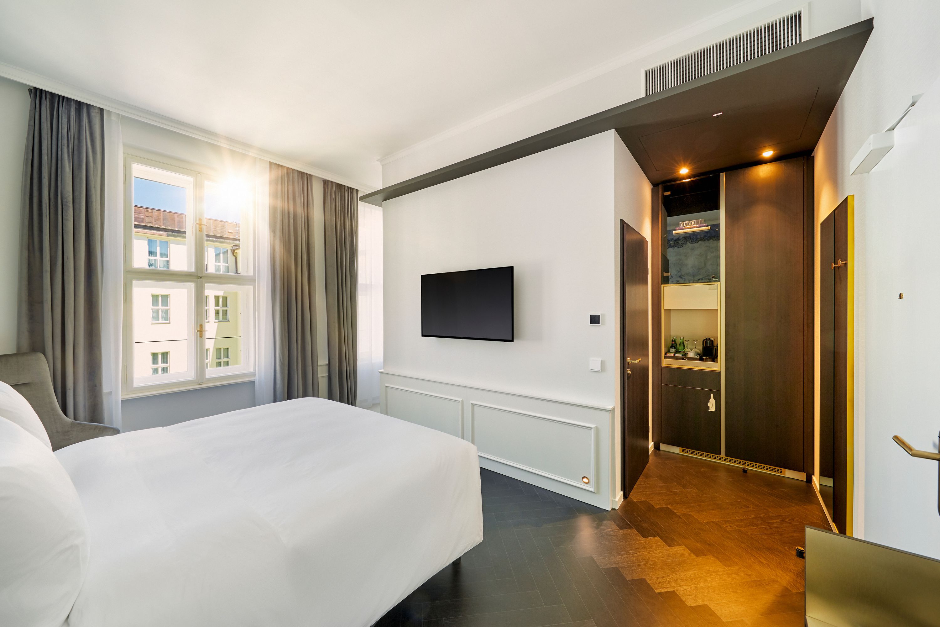 Helles Hotelzimmer mit großem Fenster, Tageslicht, komfortablem Doppelbett, moderner Wand-TV und elegantem Eingangsbereich mit Holzfußboden und indirekter Beleuchtung.