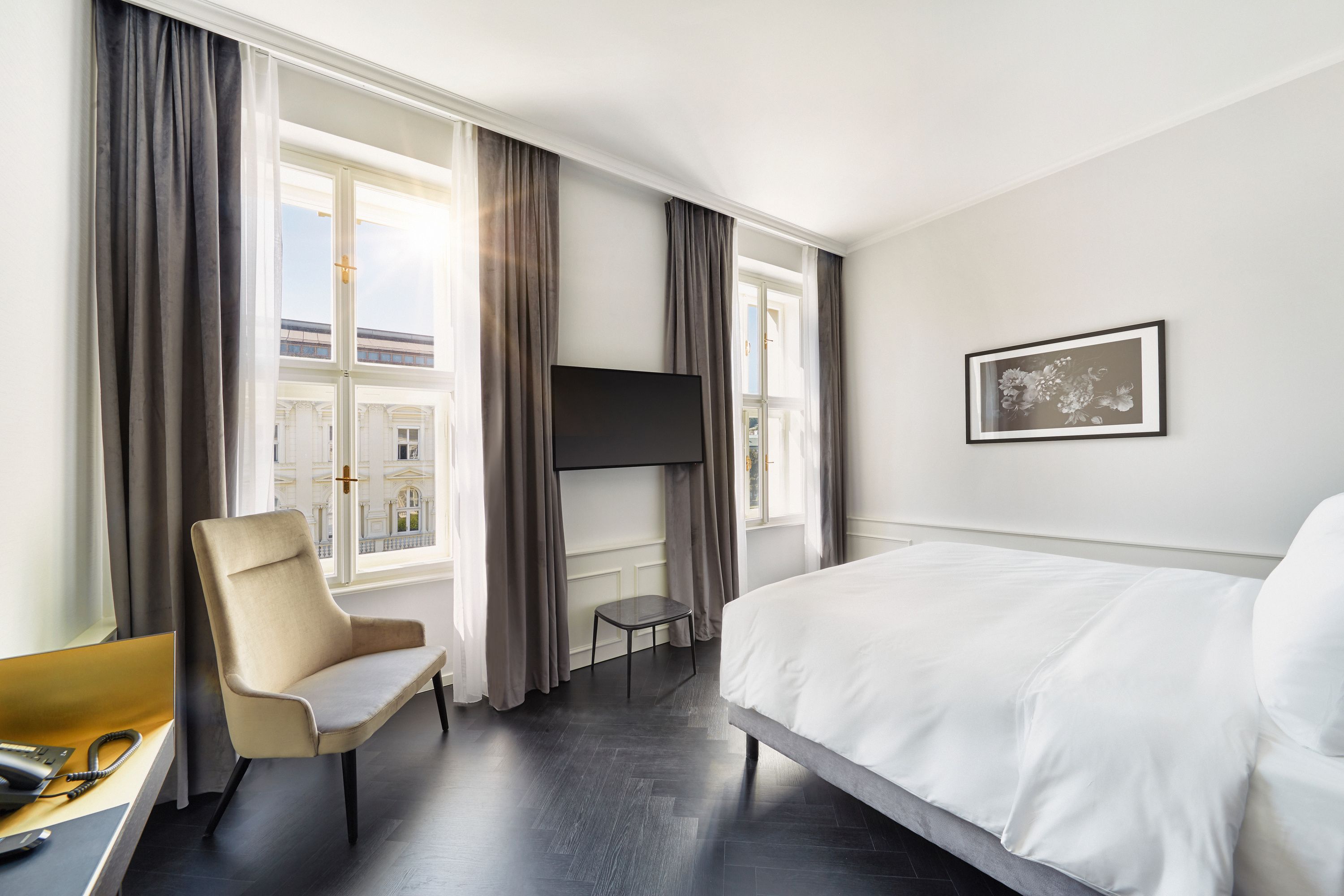 Helles, modernes Hotelzimmer mit großem Fenster, komfortablem Bett, Sessel, Flachbildfernseher und minimalistischer Ausstattung für erholsamen Aufenthalt.