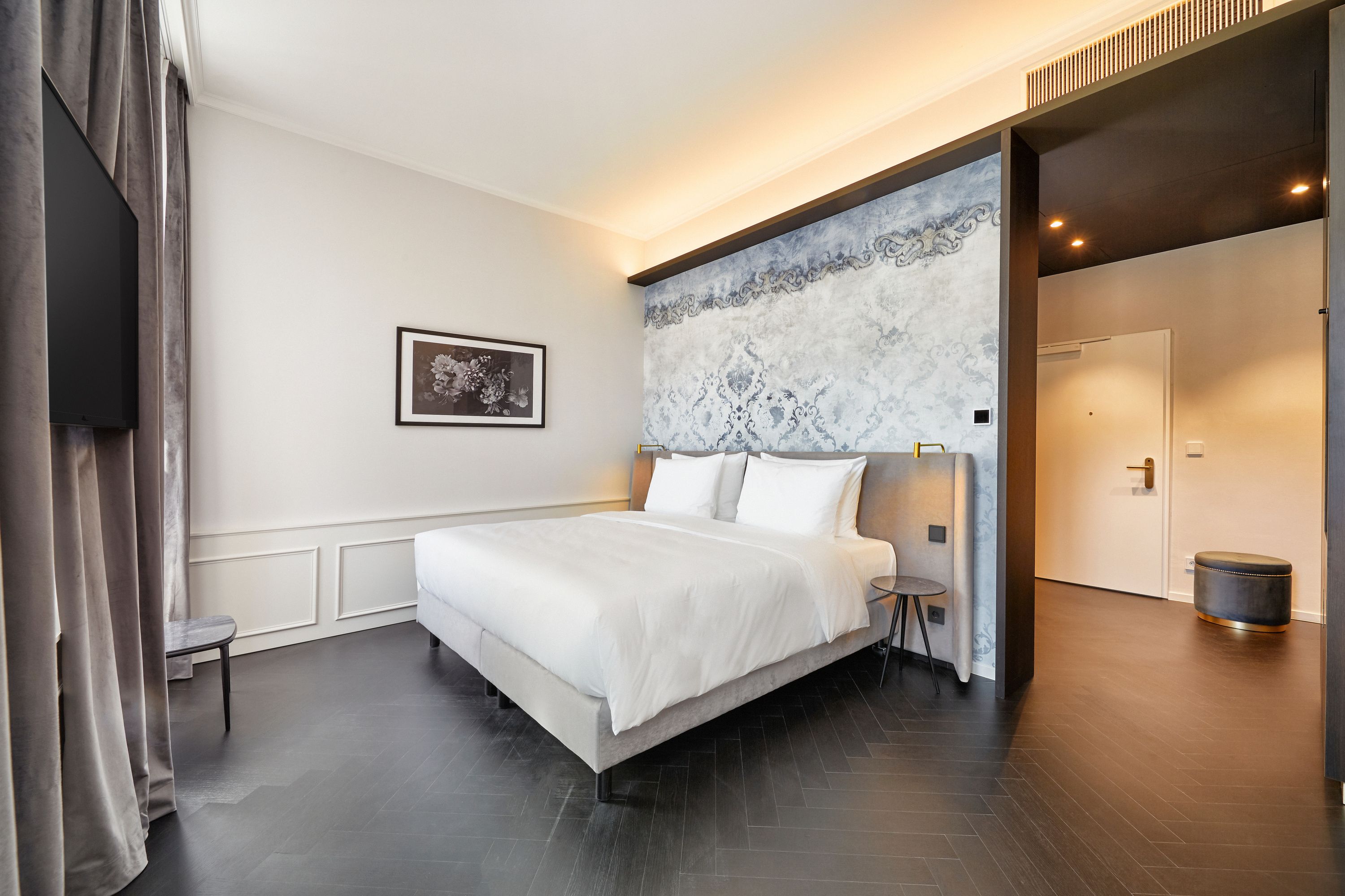 Modernes Hotelzimmer mit großem, weiß bezogenem Doppelbett, stilvoller Wandgestaltung und indirekter Beleuchtung. Helle, ruhige Atmosphäre ideal für Erholung.