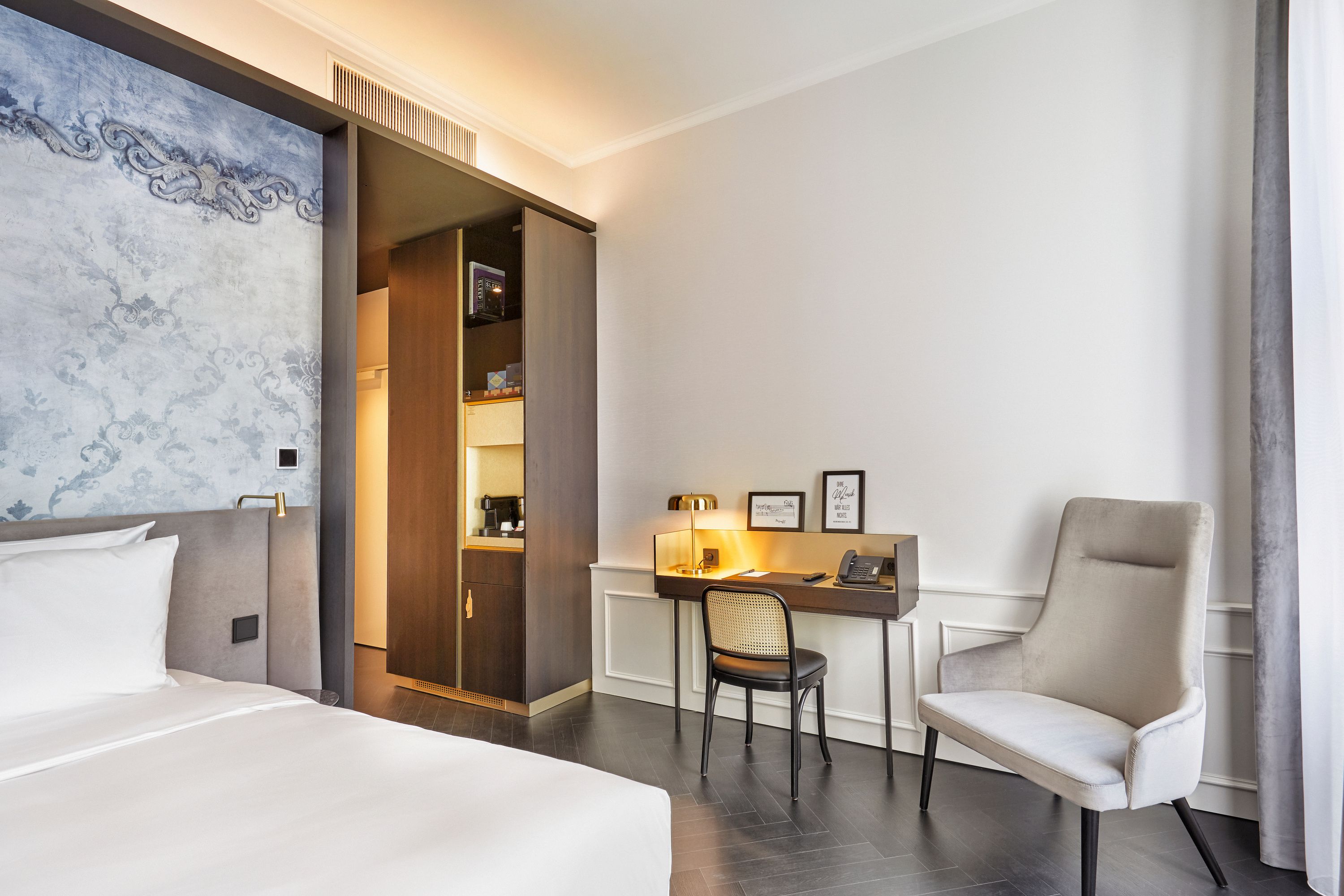 Modern eingerichtetes Hotelzimmer mit großem Bett, Schreibtisch, angenehmer Beleuchtung und gemütlichem Sessel, das eine ruhige und komfortable Atmosphäre für Arbeit und Entspannung bietet.