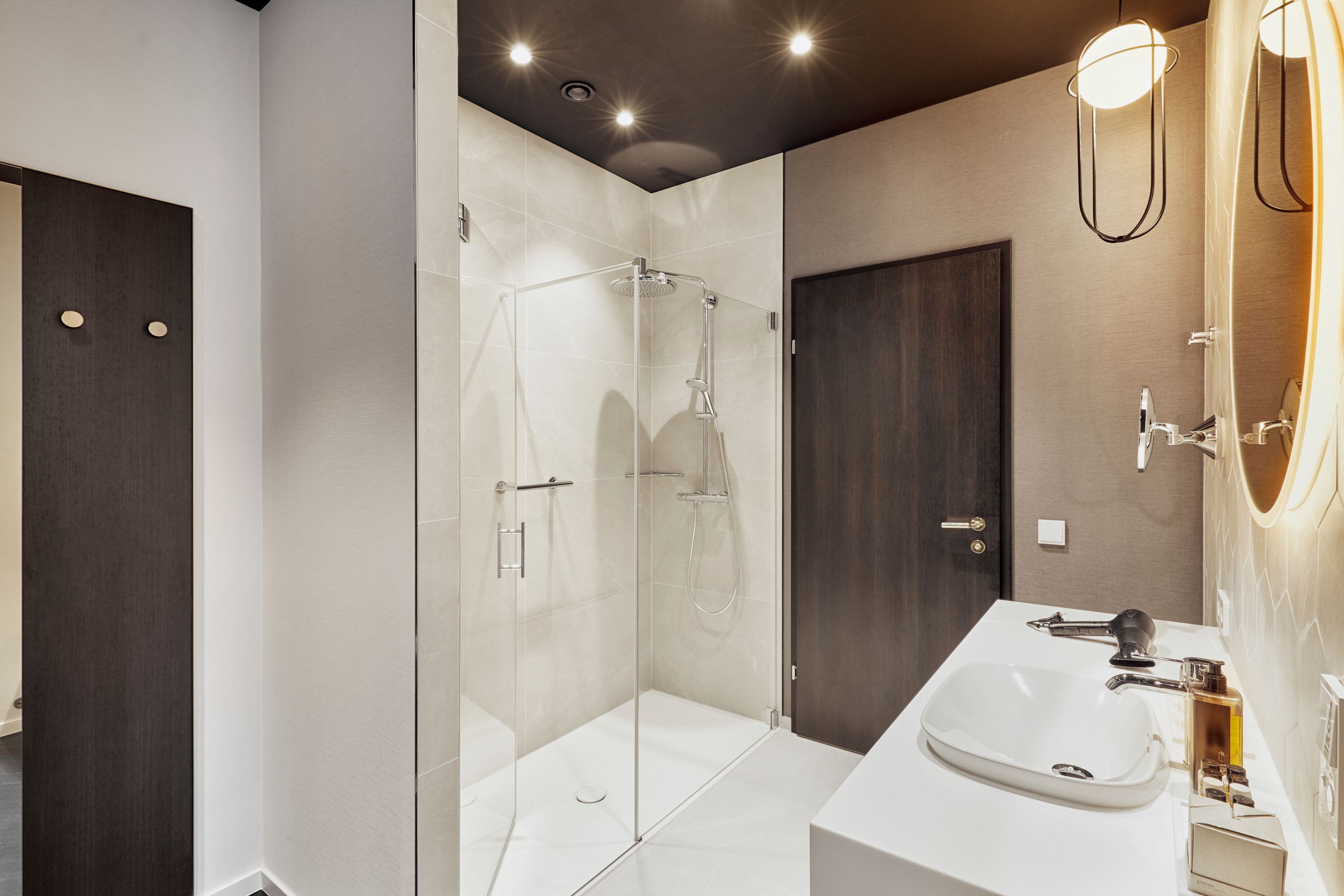 Moderner Hotelbadezimmer mit großzügiger Glasdusche, elegantem Waschbecken, beleuchtetem Spiegel und warmem, einladendem Licht für komfortable und stilvolle Entspannung.