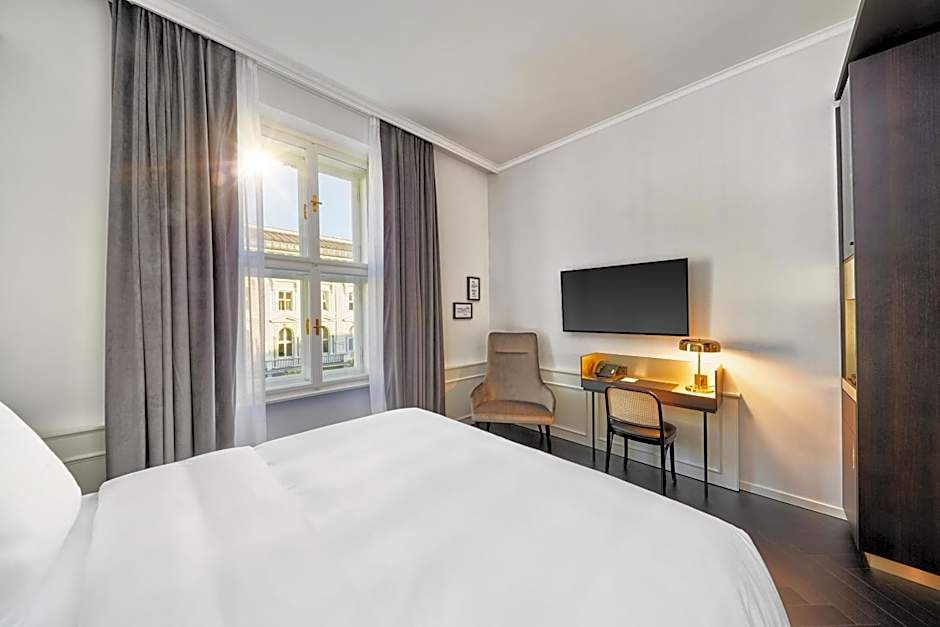 Modernes Hotelzimmer mit großem Fenster, hellem Tageslicht, gemütlichem Bett, Arbeitsplatz mit Stuhl und Fernseher sowie ruhiger, freundlicher Atmosphäre für komfortablen Aufenthalt.