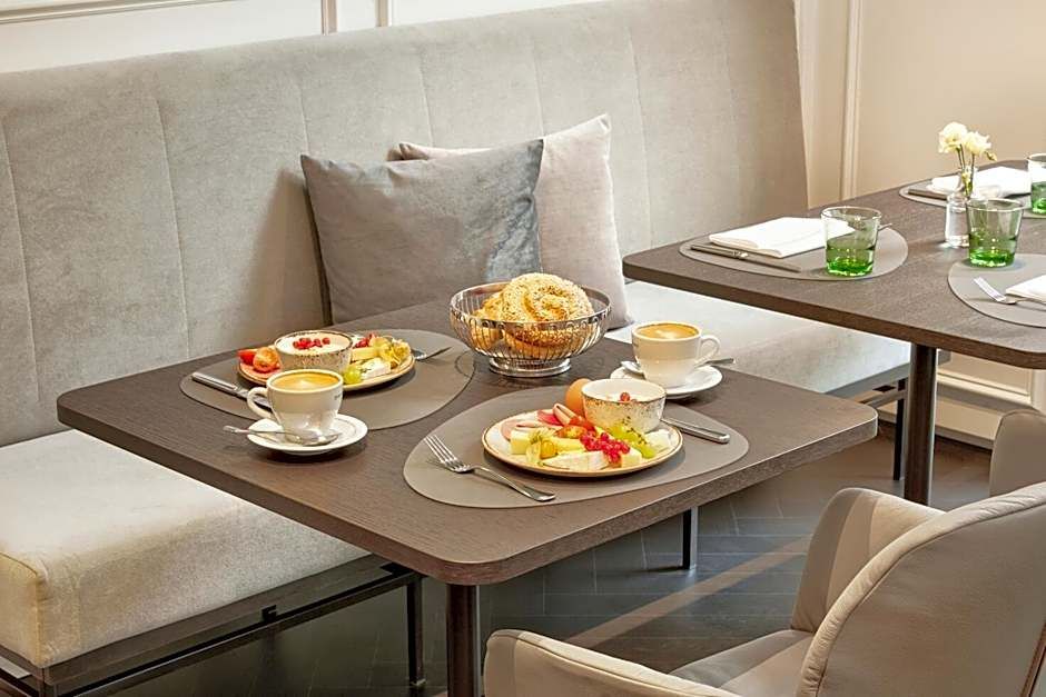 Gemütlicher Frühstückstisch mit gedeckten Tellern, frischem Obst, Brötchen in einer Schale und zwei Tassen Kaffee in einem hellen, modernen Essbereich.