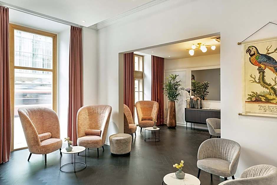 Heller Lounge-Bereich mit bequemen Sesseln und kleinen Tischen, großen Fenstern mit Vorhängen, elegantem Boden und freundlicher Atmosphäre für entspannte Gespräche oder Wartezeiten.