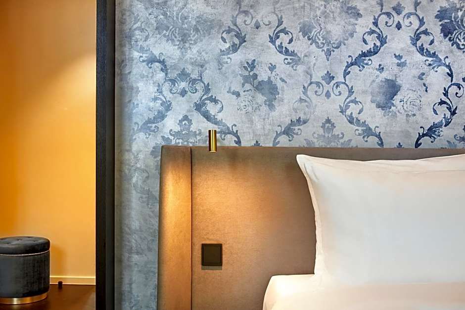 Elegantes Hotelzimmer mit gemütlichem, gepolstertem Kopfteil, weißem Kissen und stilvoller blauer Tapete im Hintergrund. Warme Beleuchtung schafft ein einladendes Ambiente.