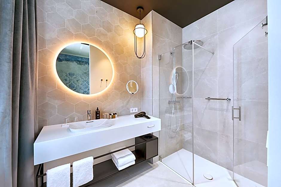 Modernes Badezimmer mit großem, beleuchtetem Rundspiegel, weißem Waschtisch, Regendusche mit Glasabtrennung und hellem, fliesenbedecktem Ambiente für angenehmen Komfort und Entspannung.
