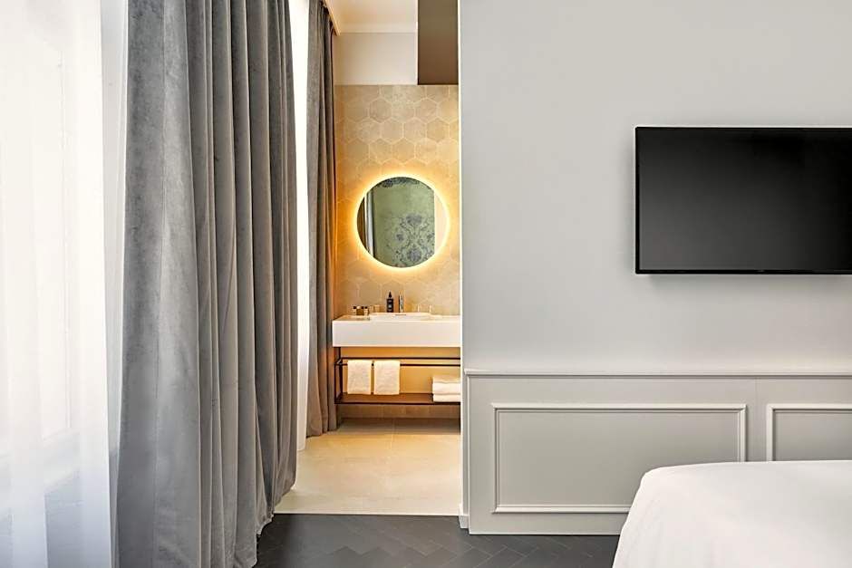 Modernes Hotelzimmer mit elegantem, hell beleuchtetem Badezimmer, rundem Spiegel, flauschigen Handtüchern und elegantem Fernseher, das ruhige Atmosphäre und Komfort ausstrahlt.