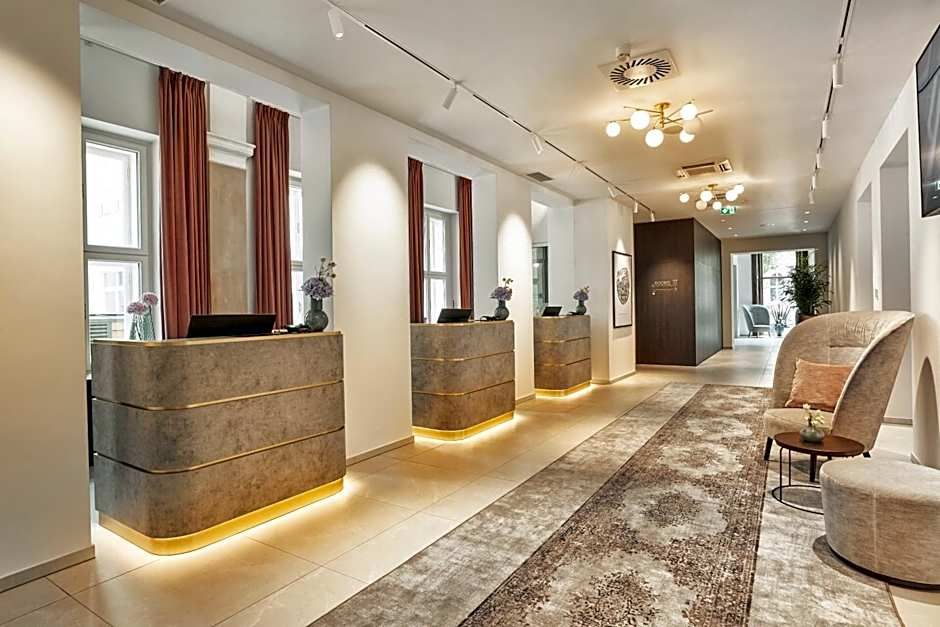 Heller und moderner Hotel-Empfangsbereich mit mehreren Tresen, warmen Lichtakzenten, komfortablen Sitzmöglichkeiten und großem Teppichläufer, der zu einem einladenden Aufenthaltsbereich führt.