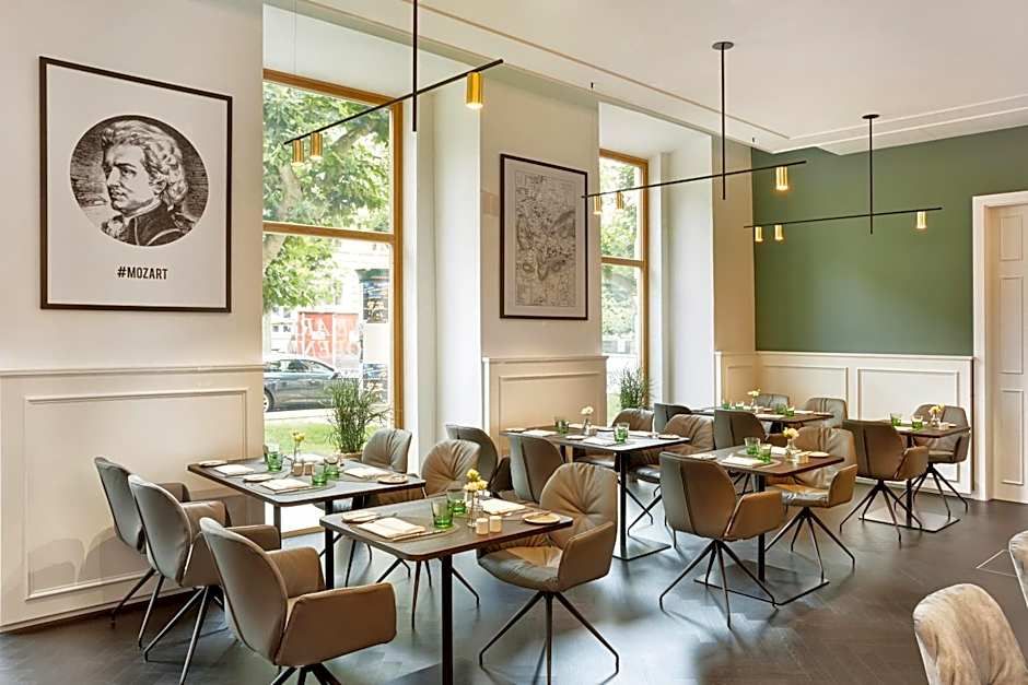 Modern eingerichteter Speiseraum mit großen Fenstern, grüner Akzentwand und bequemen Polstersesseln. Tischdekoration mit kleinen Vasen schafft ein einladendes Ambiente zum entspannten Essen.